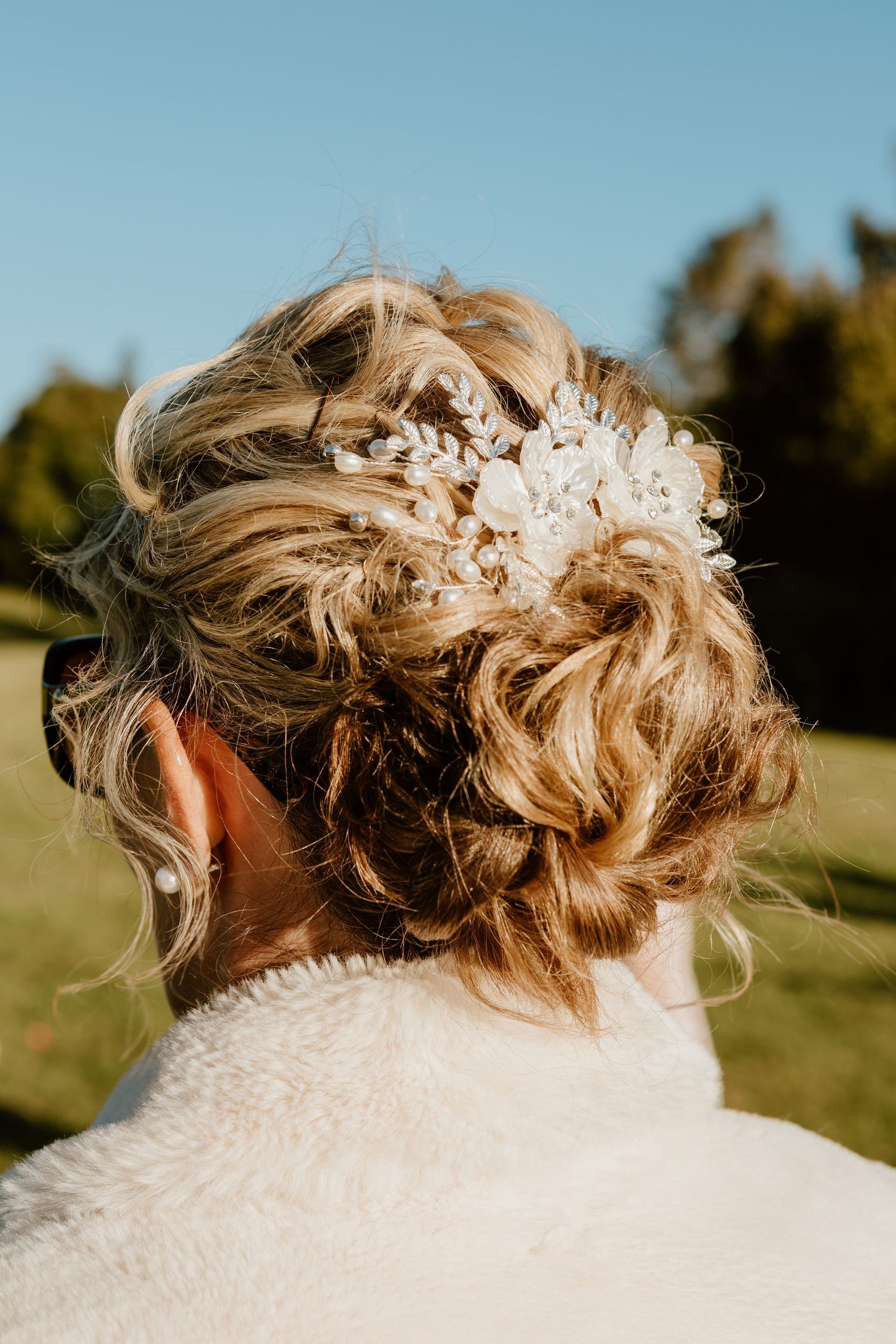 Close-up view of elegant bridal updo hairstyle with delicate white floral hair accessories against outdoor background.