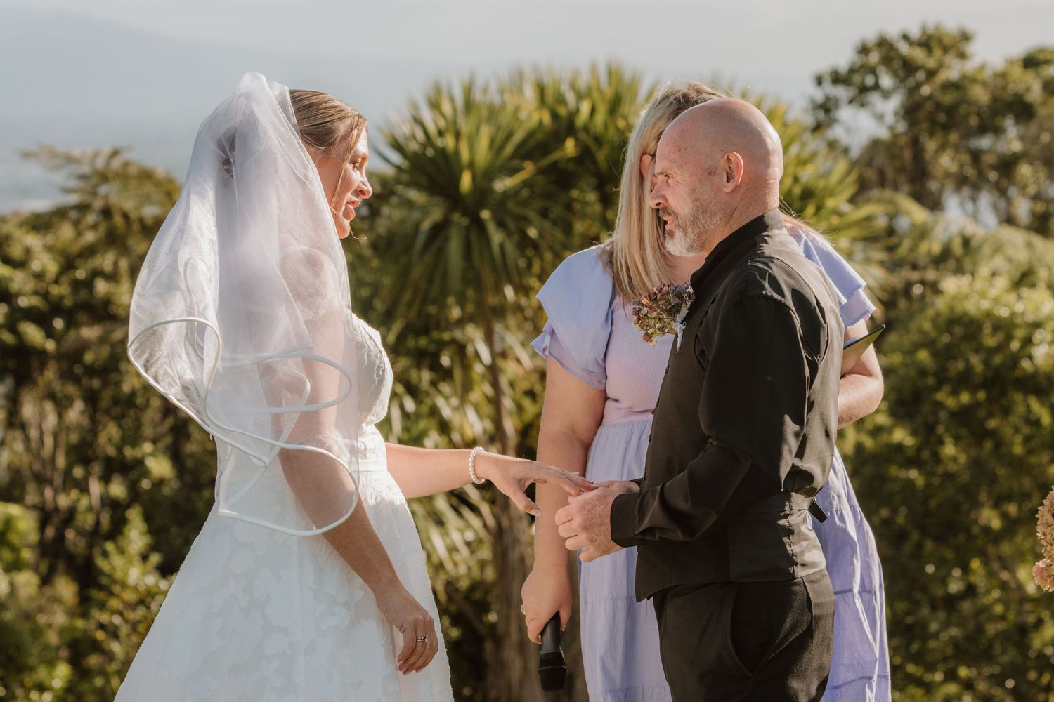 Wedding ceremony taking place outdoors on a sunny day with a minister officiating the service.
