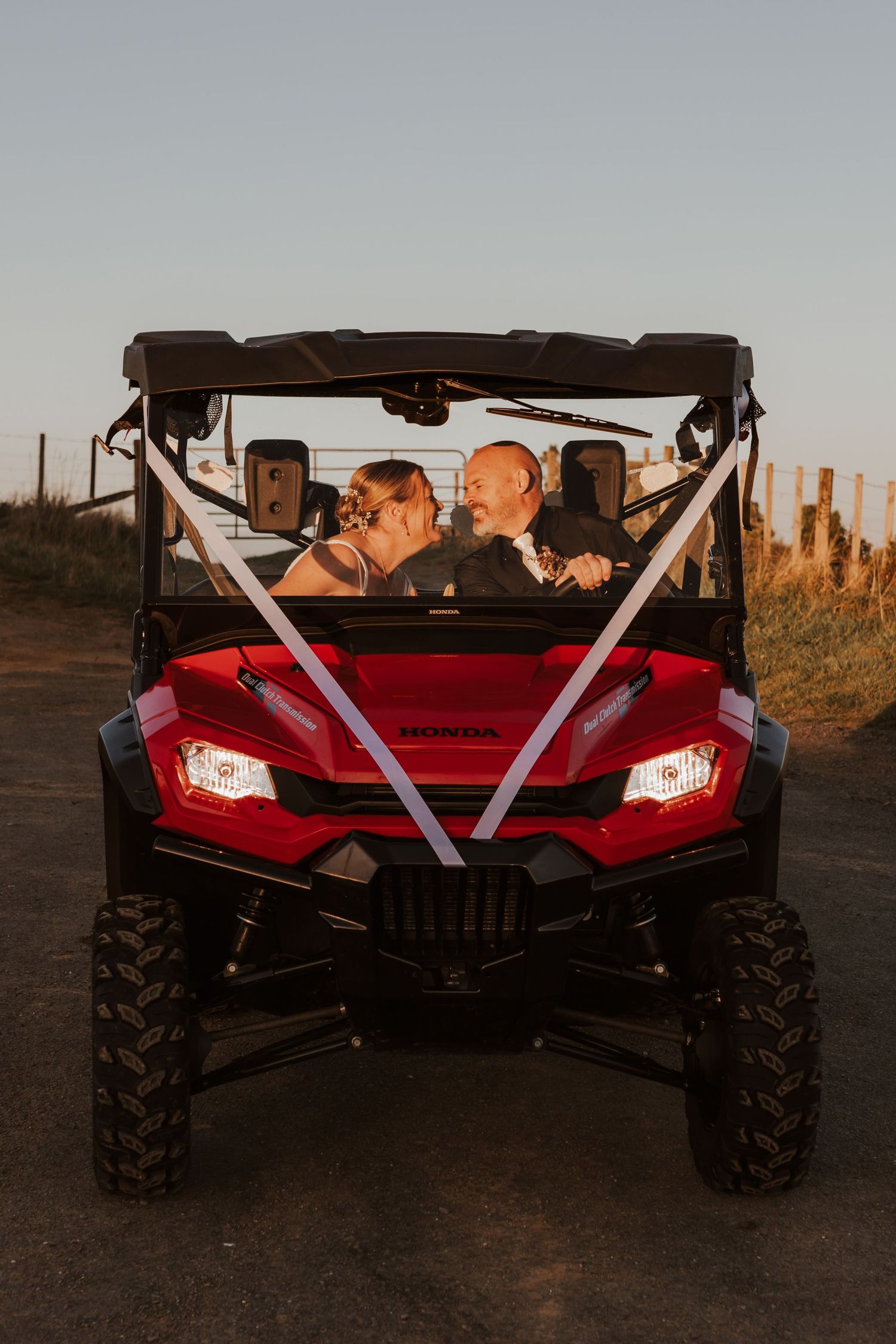 Red utility vehicle with couple seated inside at sunset with desert landscape in background.