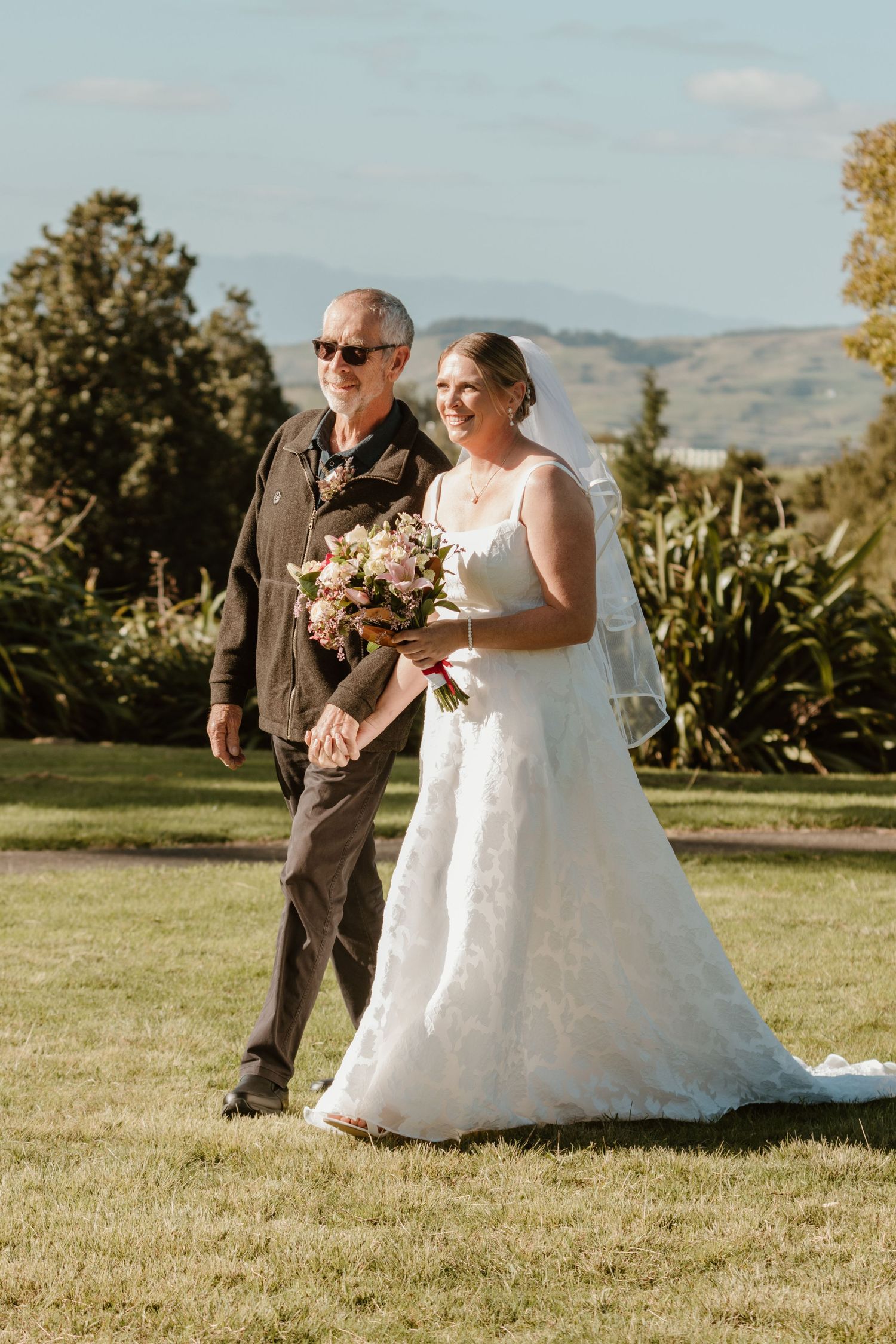 Two people walking on a grassy lawn at an outdoor wedding ceremony with mountains visible in the background.