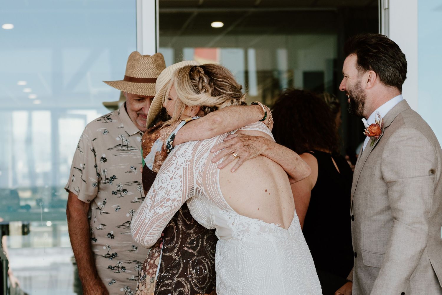 Wedding party members sharing emotional moments in a bright indoor venue. Papamoa Surf Lifesaving Club Wedding