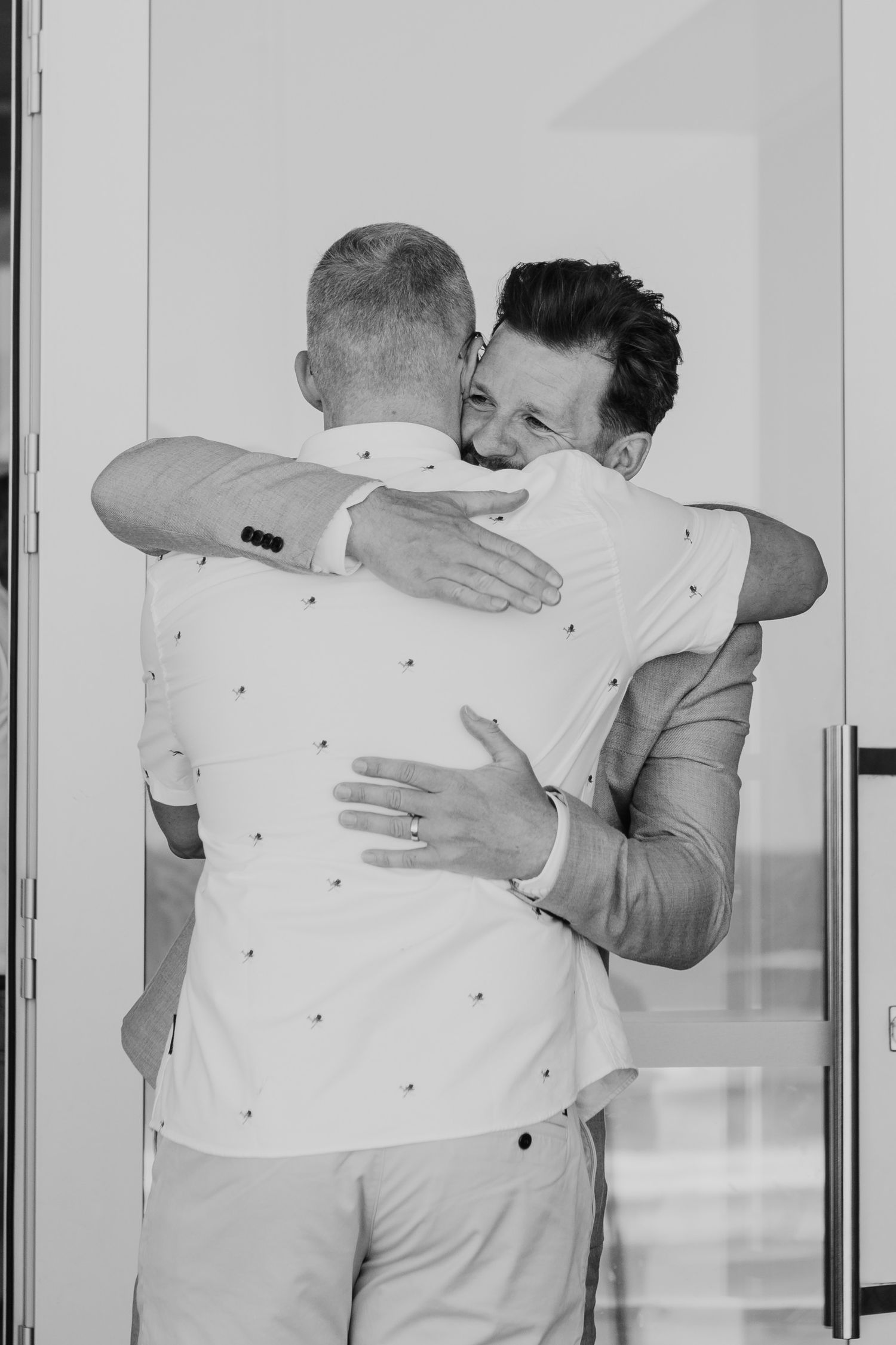 Emotional group embrace captured in black and white during wedding celebration. Papamoa Beach Wedding