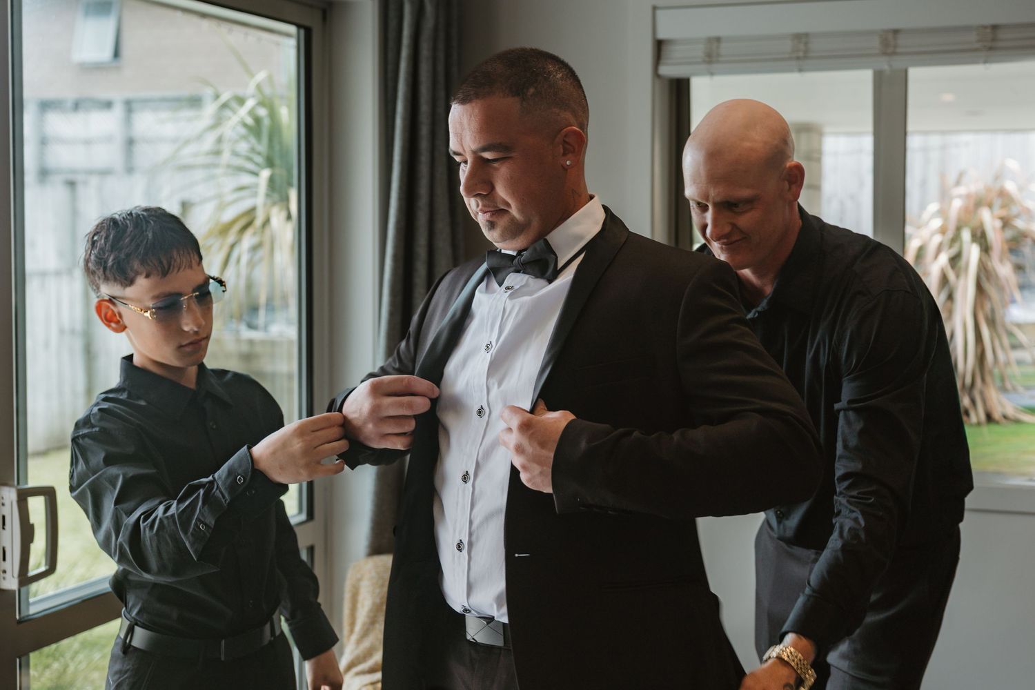 A group of formally dressed people in black suits gather in a bright indoor space.