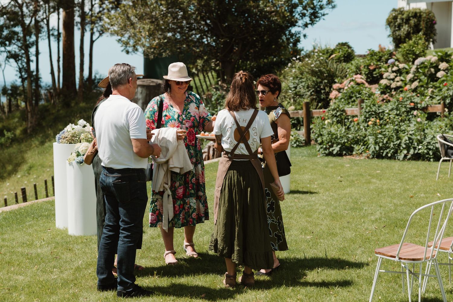 Four guests socializing on a lush green lawn at an outdoor garden wedding reception on a sunny day.