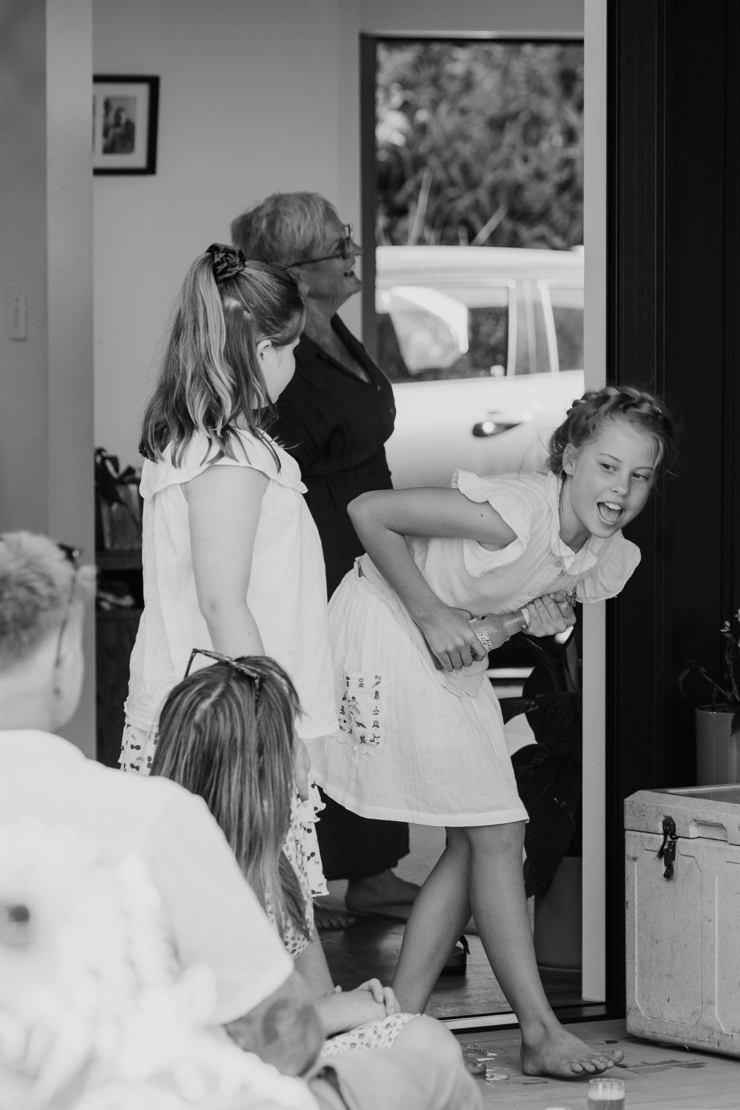 Black and white photo of children playing and laughing in doorway during a wedding preparation scene.