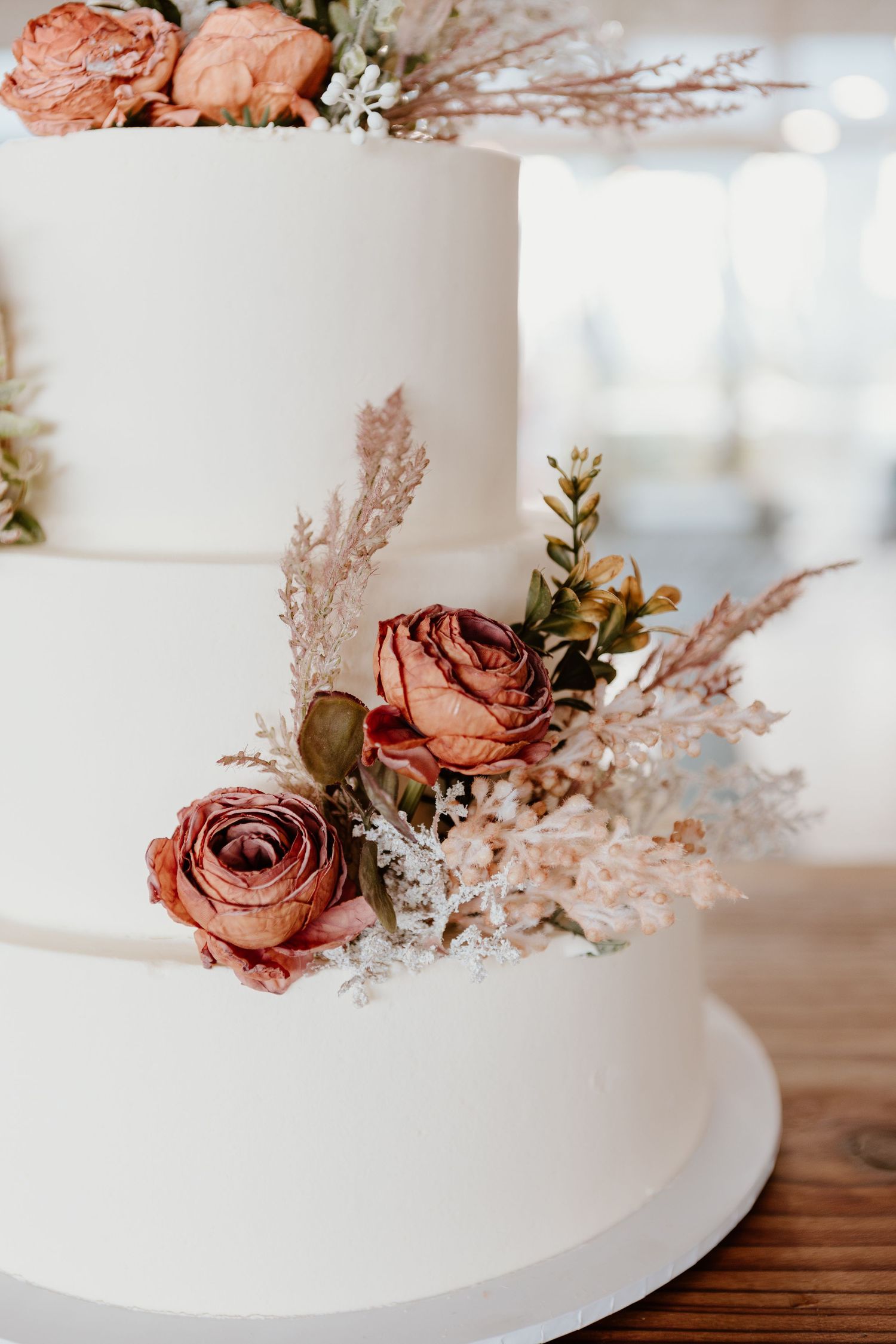 Elegant white wedding cake decorated with dried pink roses and delicate pampas grass floral accents.