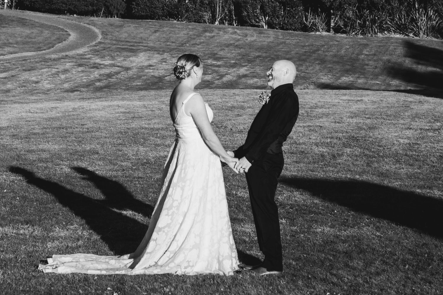 A black and white wedding photo shows a bride in a flowing gown and groom standing back to back on a grassy hill.