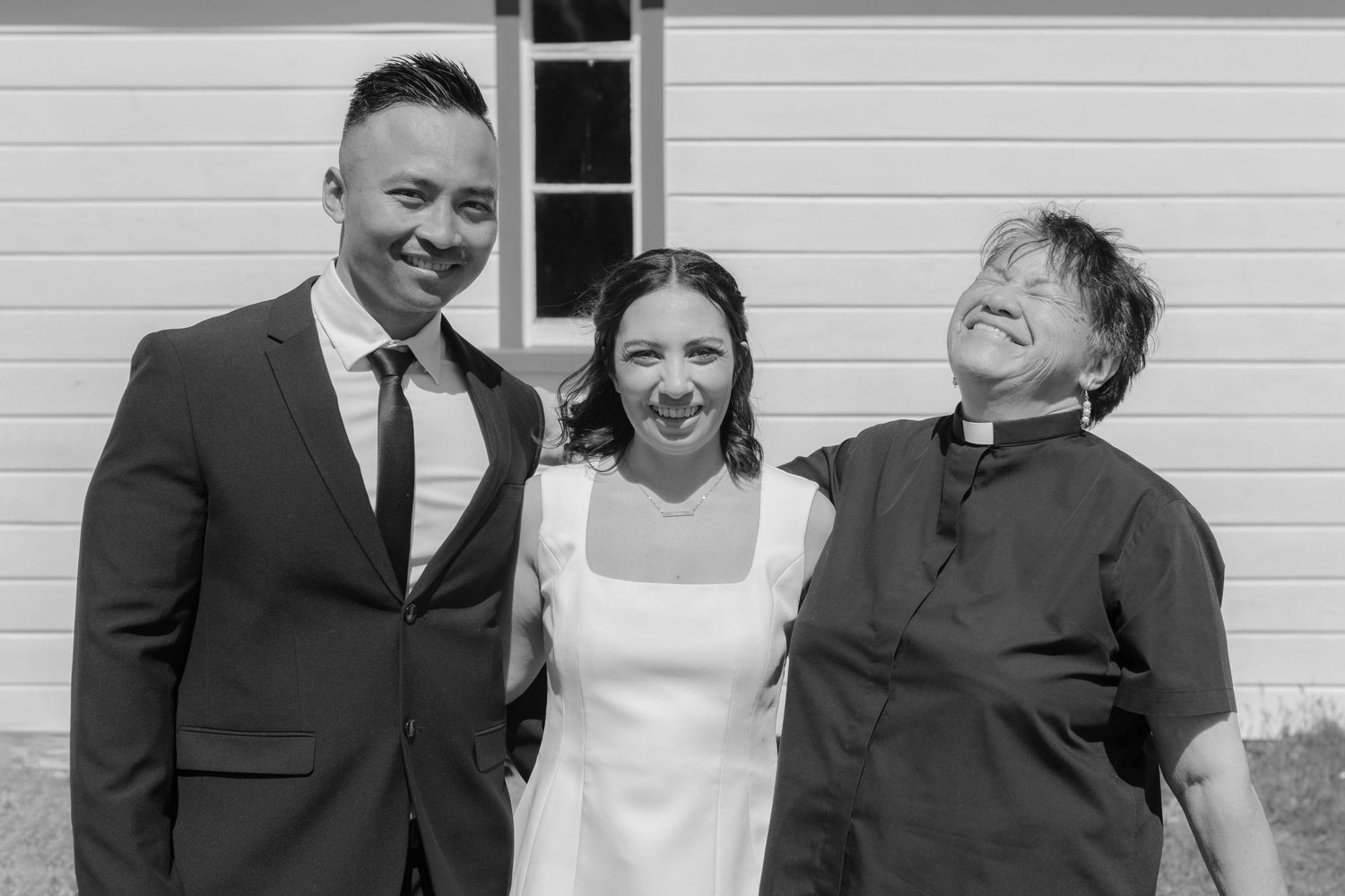 Black and white portrait of a wedding party posing in front of a white building.