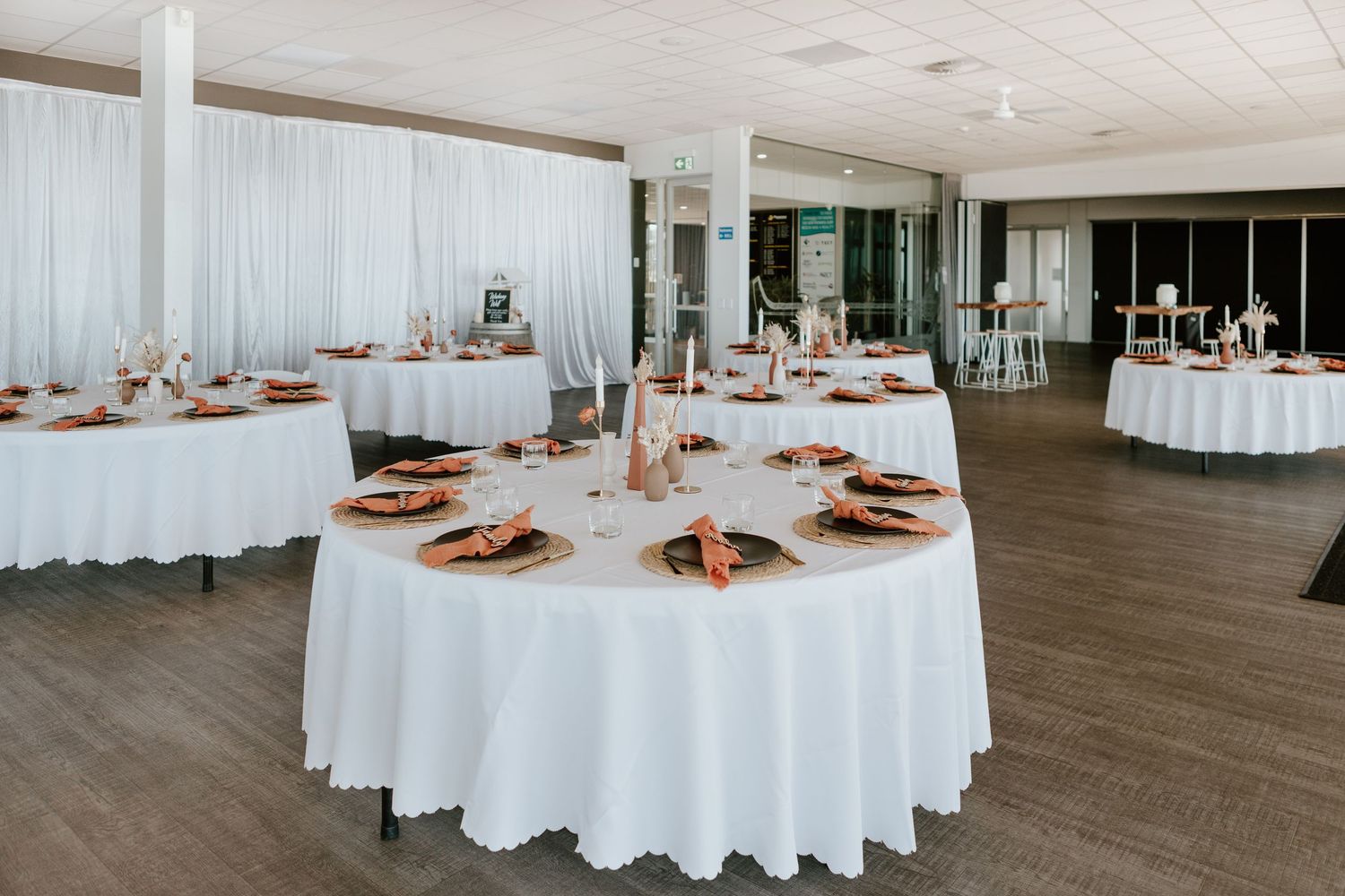 Event venue setup with elegant round tables covered in white linens and ornate place settings.