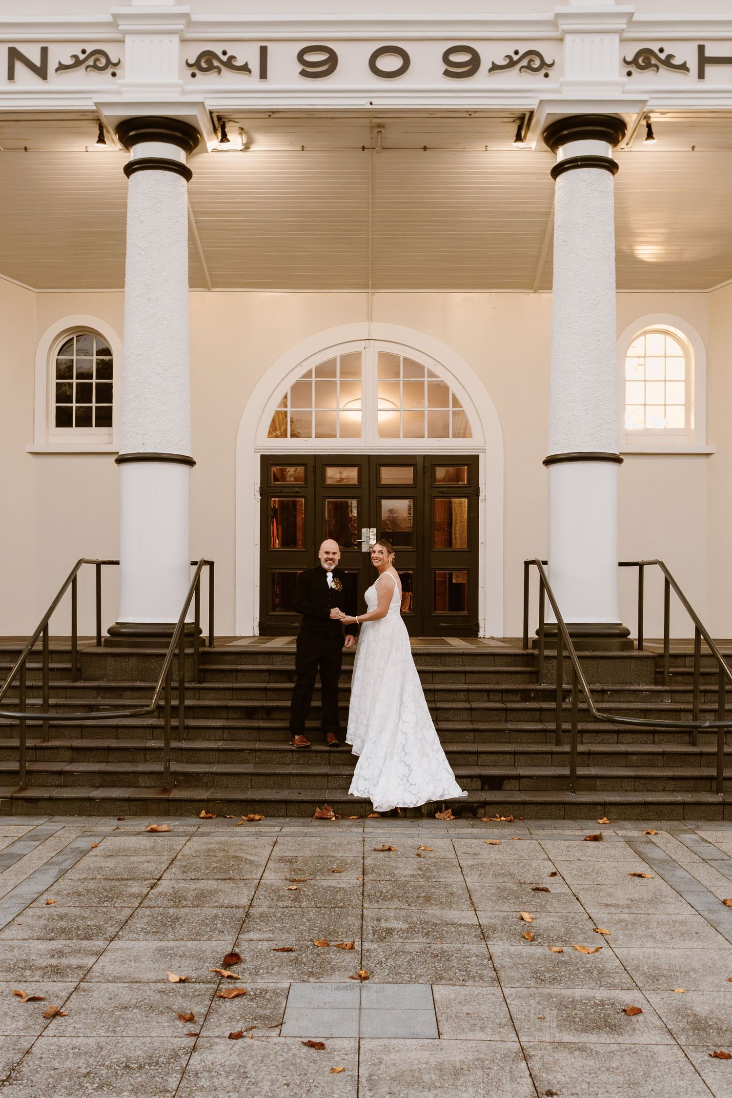 A couple stands outside a historic white building with columns and arched windows at dusk.