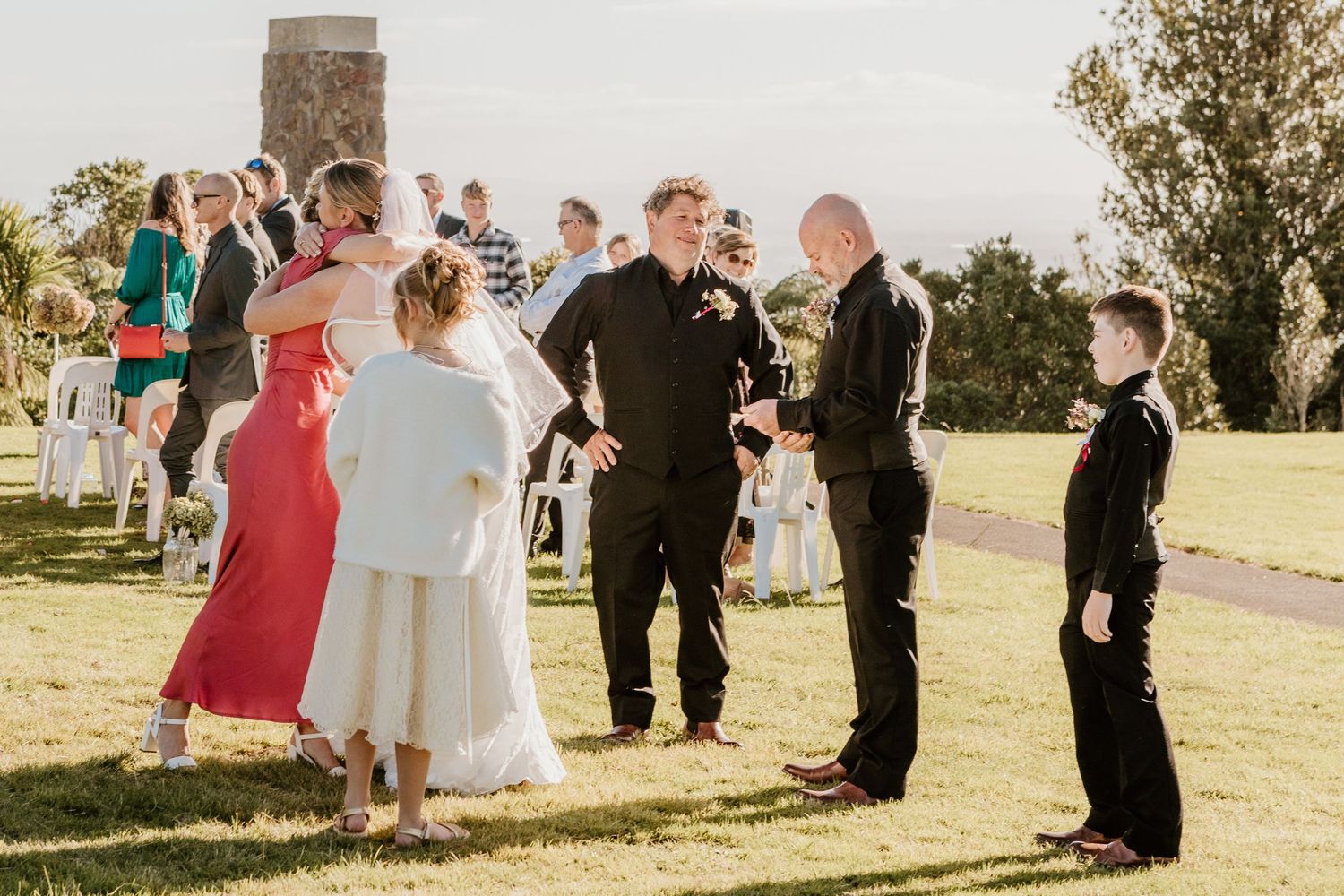 A sequence of outdoor wedding ceremony moments showing a group in formal attire standing together under natural sunlight.
