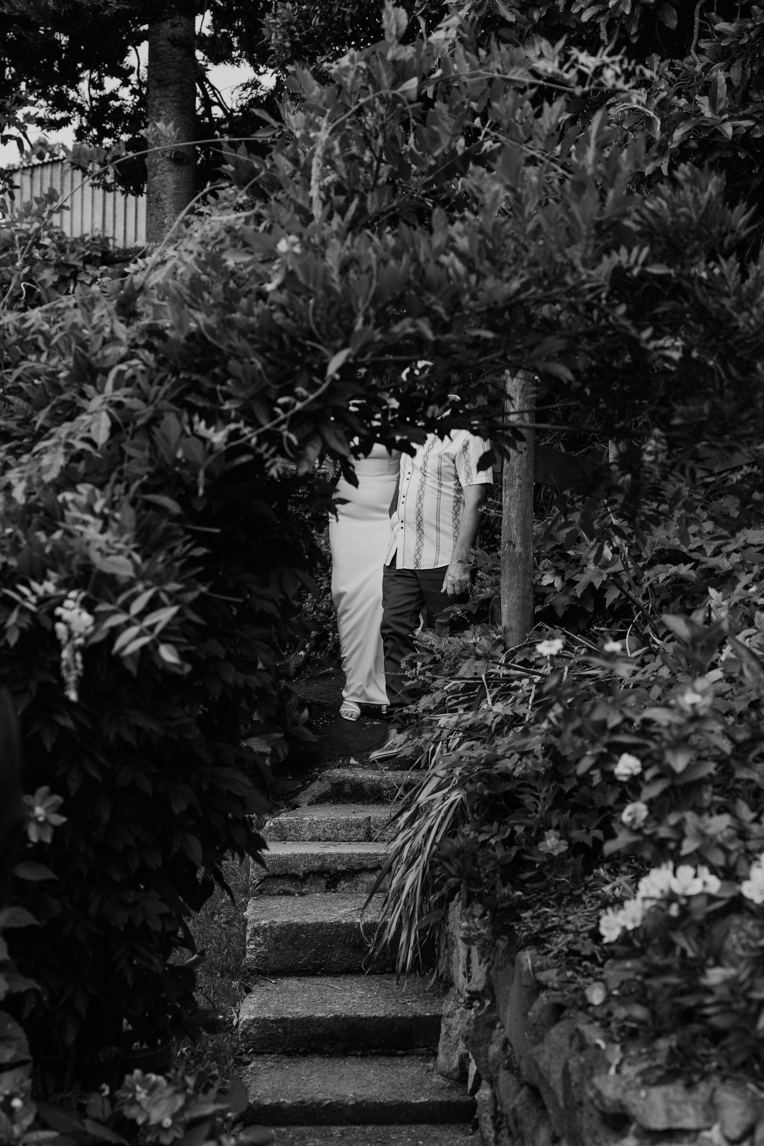 Black and white photo of a person walking up stone steps surrounded by lush garden foliage and flowering plants.