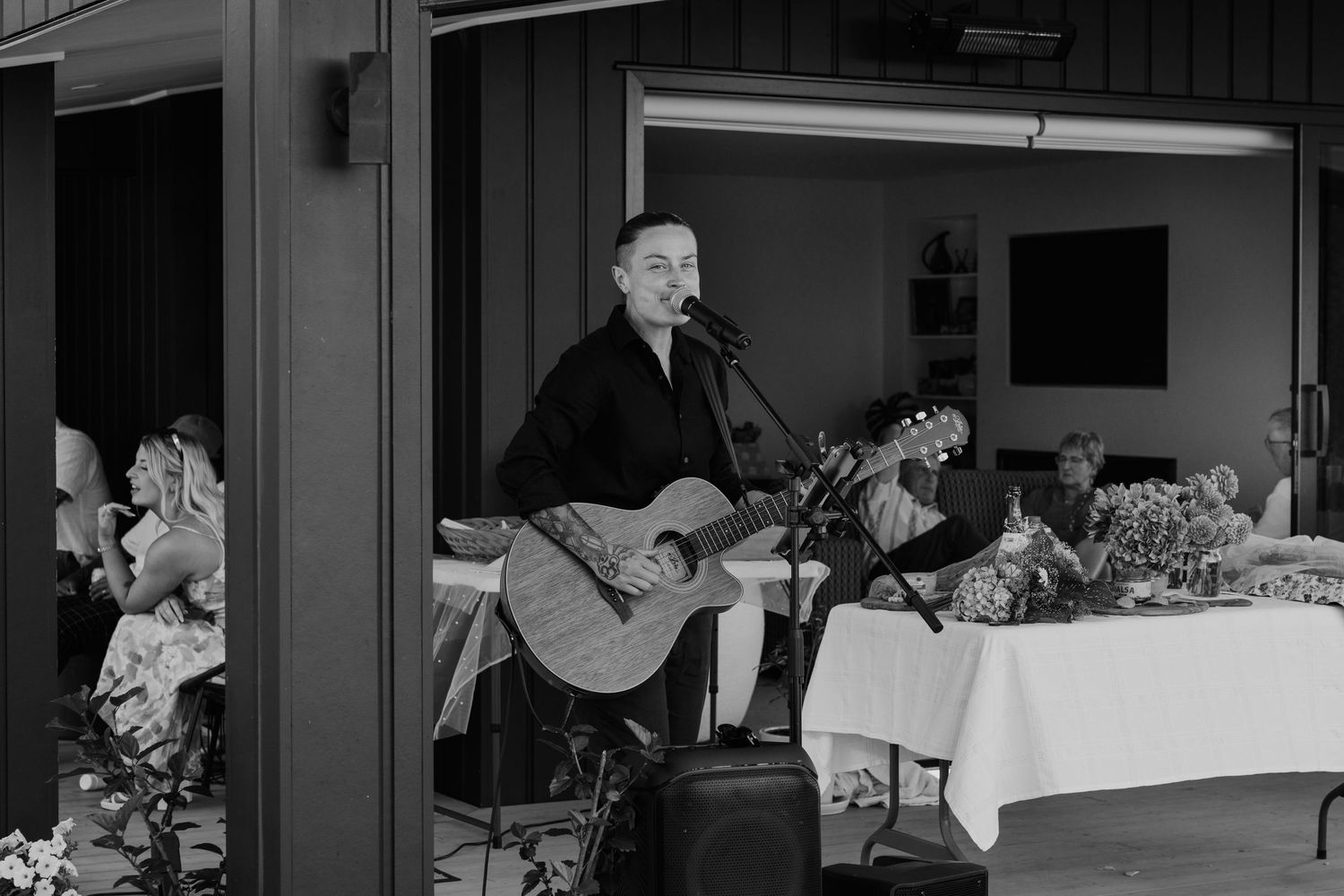 Black and white photo of a male guitarist performing acoustic set at an elegant indoor wedding reception.