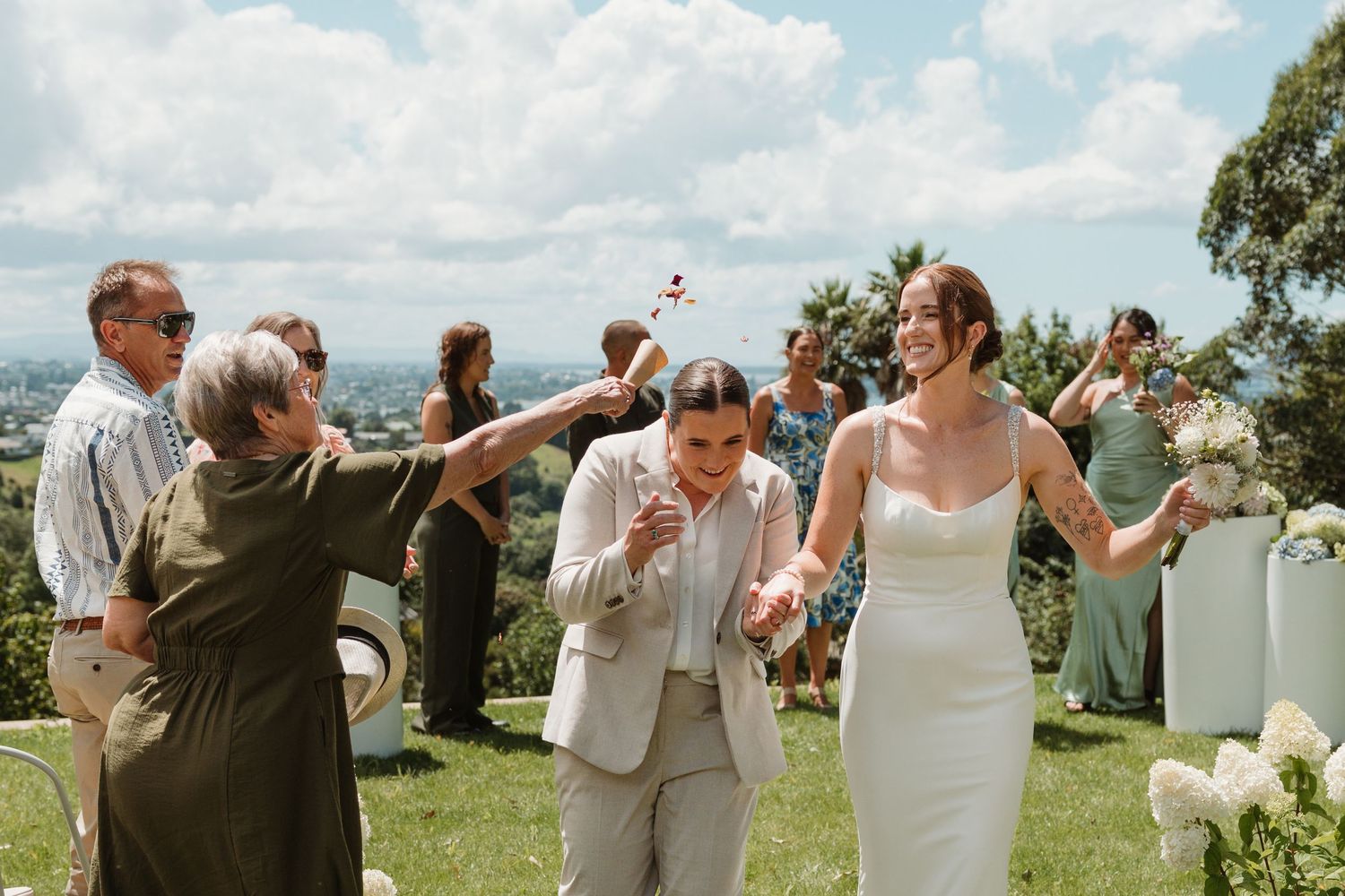 Wedding guests participate in a fun champagne spray celebration outdoors on a sunny day.