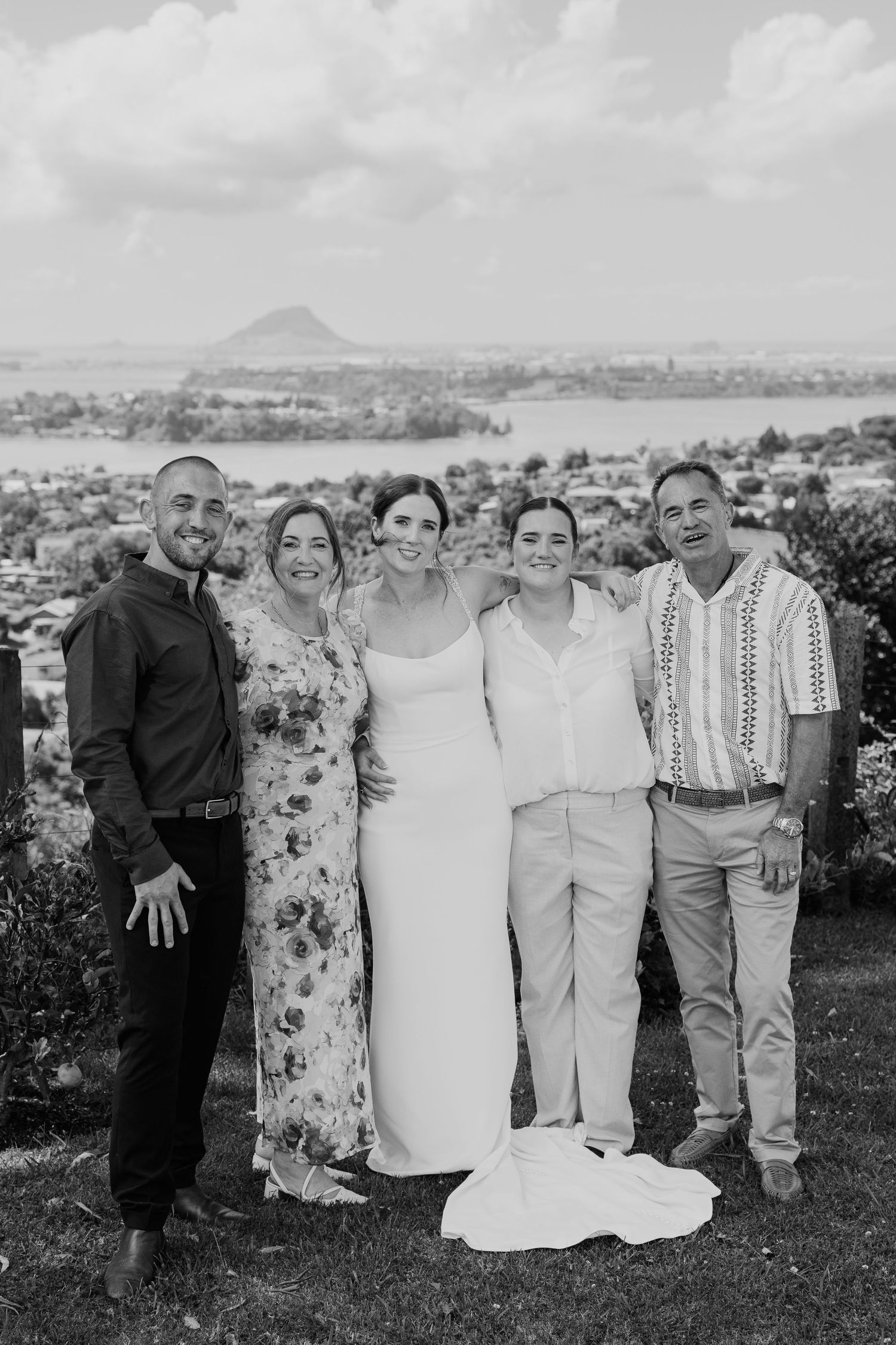 Black and white wedding photo of five people posing outdoors with scenic landscape and mountain in background.