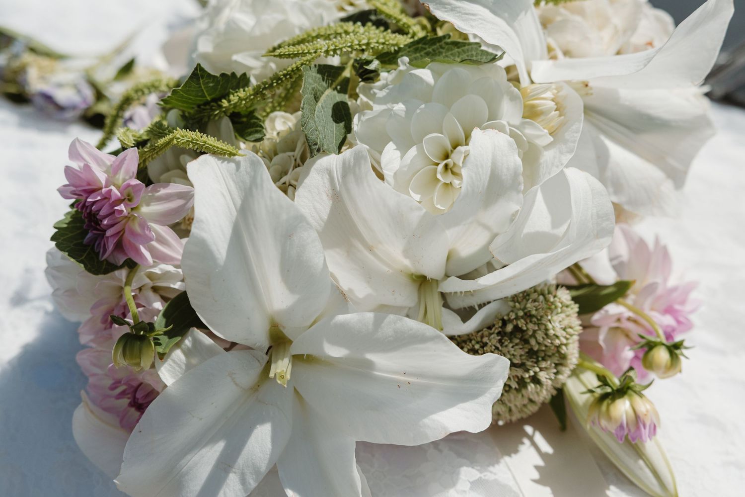 A beautiful bridal bouquet featuring white roses, magnolias, and soft pink wildflowers arranged on a white surface.