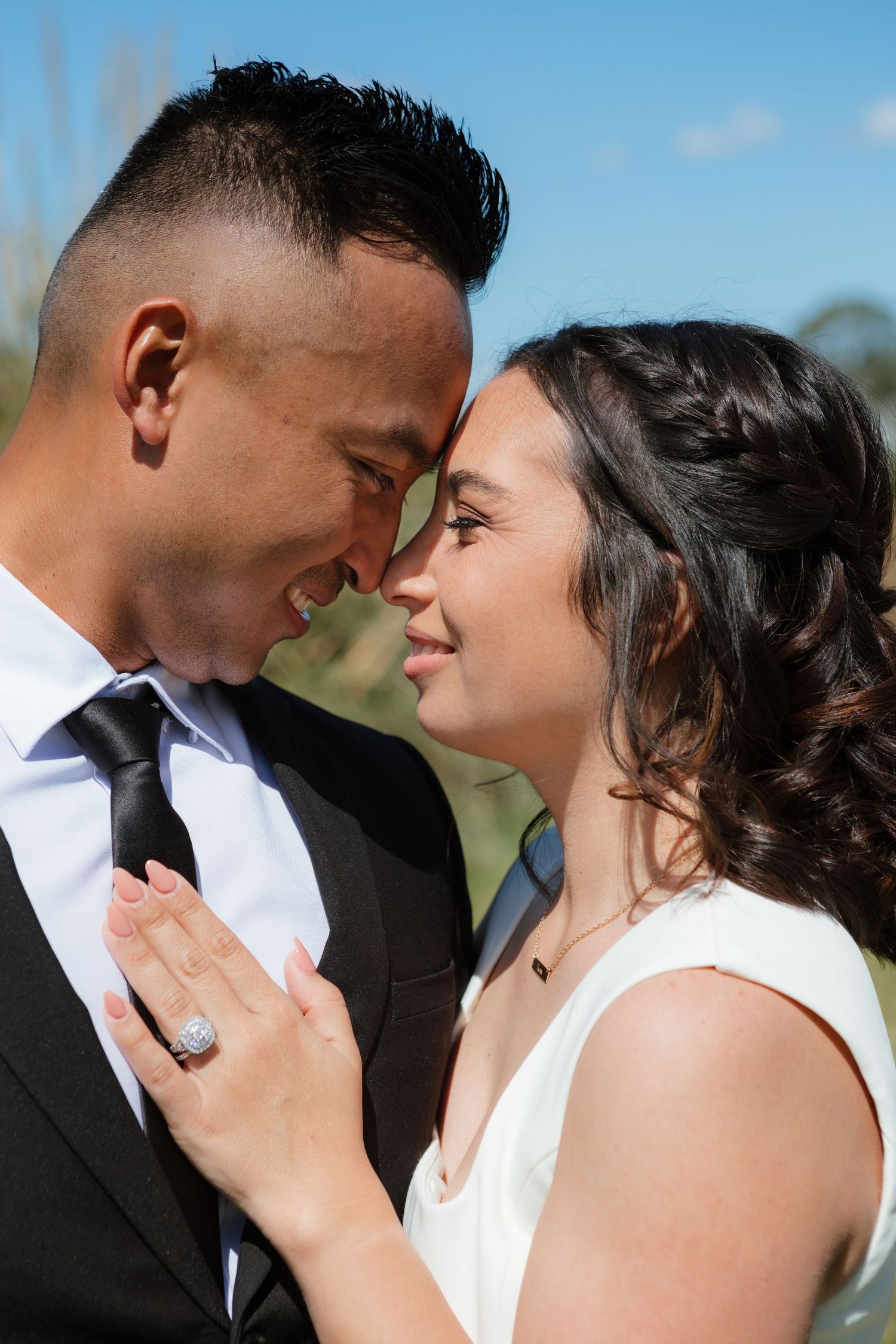 A romantic couple shares intimate moments in their wedding attire against a blurred outdoor background.