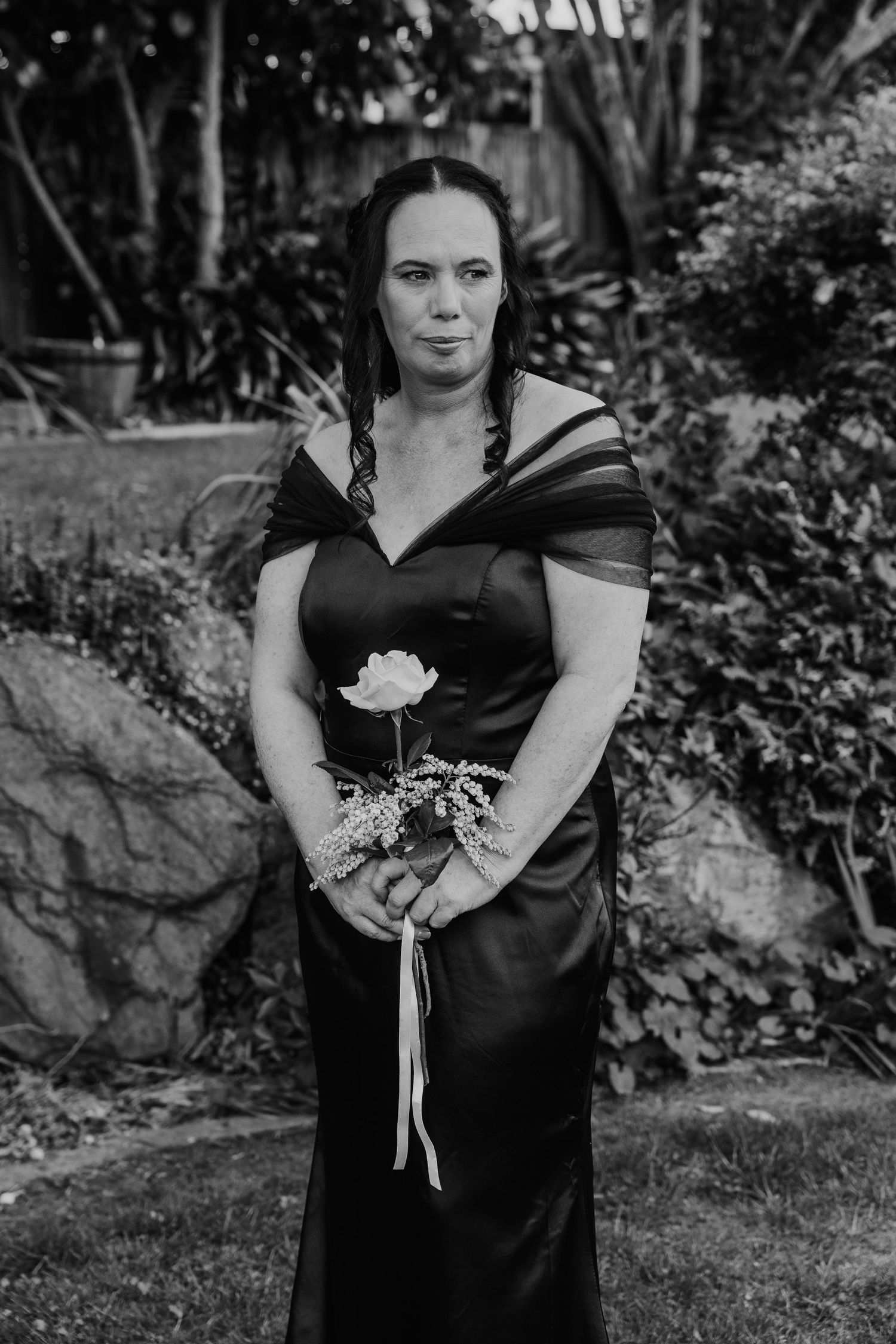 A figure in a black dress holds a white rose while posing in a garden setting across multiple black and white photos.