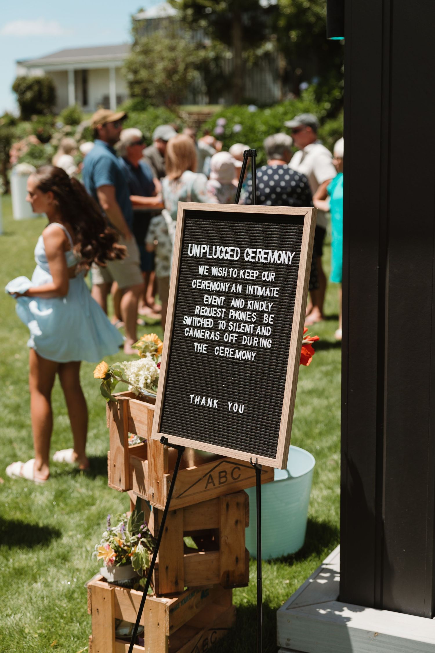 Unplugged wedding ceremony sign on wooden crates asking guests to silence phones and cameras outdoors.