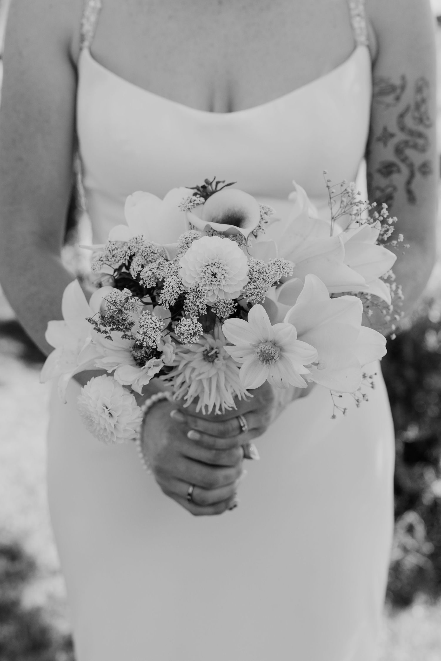 Bride in white gown holding a beautiful bouquet of mixed flowers, black and white wedding photography.