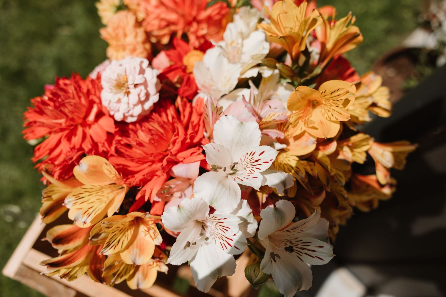Vibrant bouquet of red, orange, white, and yellow alstroemeria and dahlia flowers arranged in a wooden box.