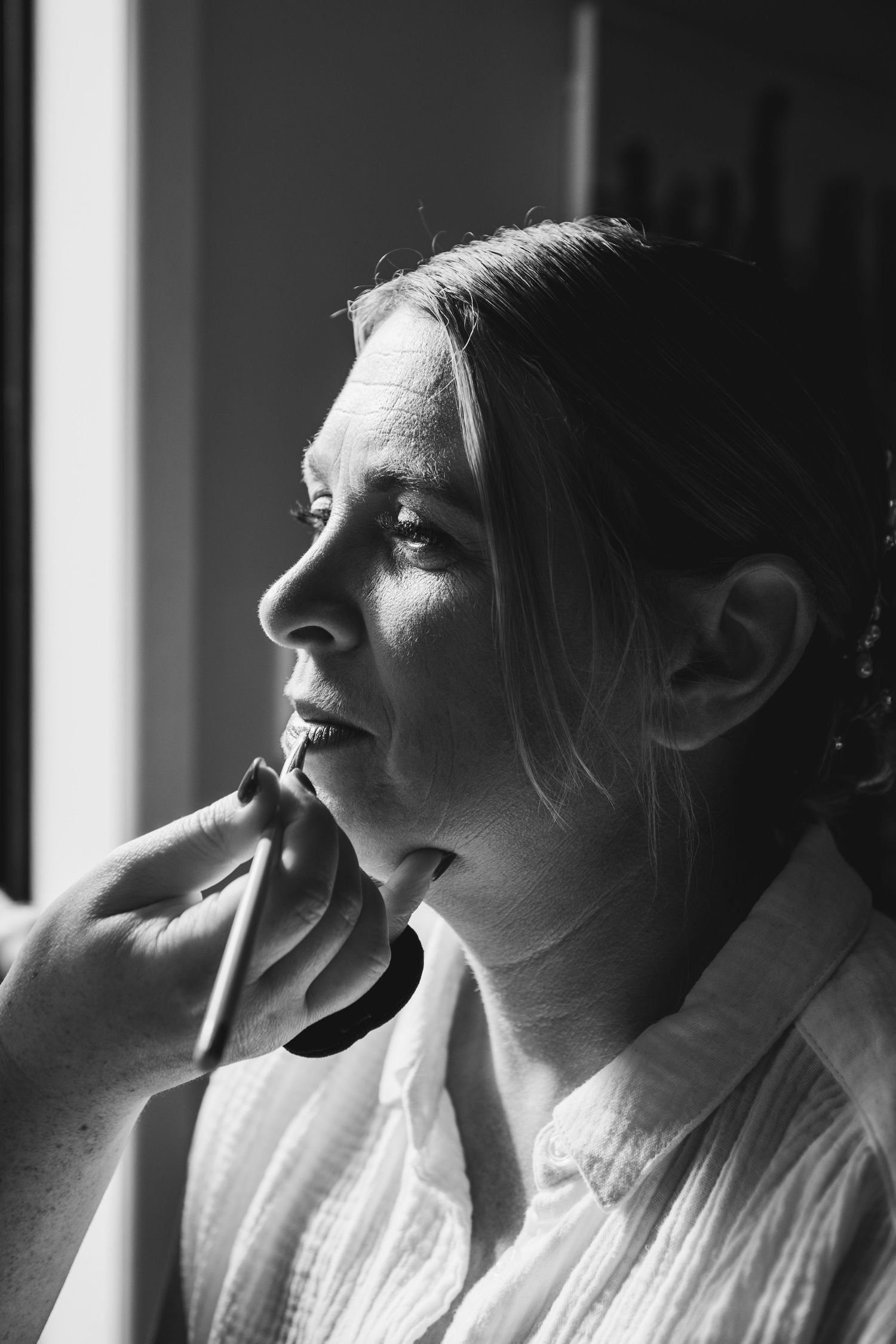 A black and white portrait of a person gazing thoughtfully by a window with natural light illuminating their profile.