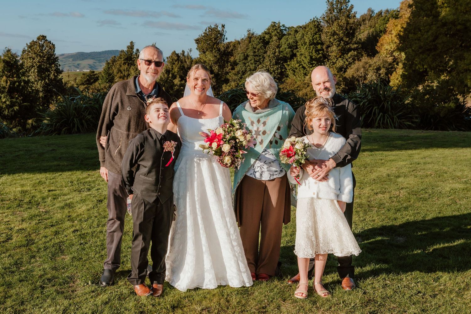 Wedding party poses outdoors in natural setting with trees and grass on sunny autumn day.