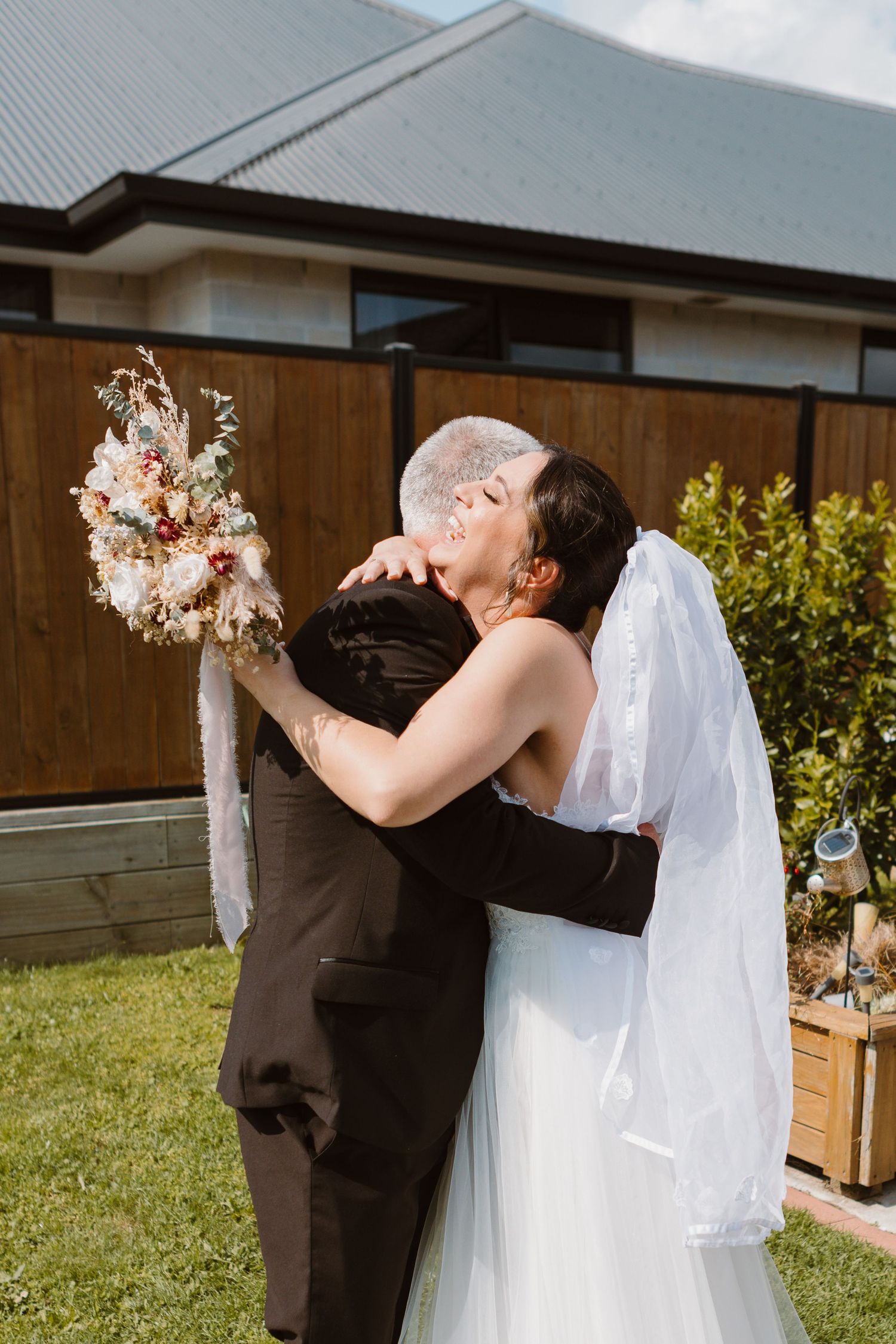 A romantic outdoor wedding moment as a couple shares their first kiss while holding a dried floral bouquet.
