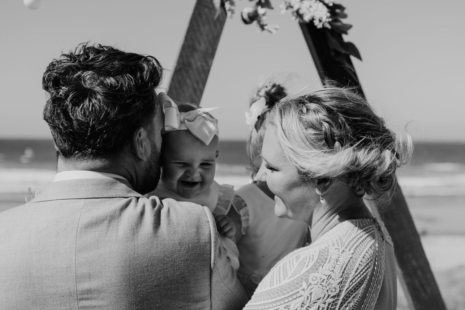A joyful moment captured during a seaside wedding ceremony under a decorated wooden arch.  Papamoa Surf Lifesaving Club Wedding