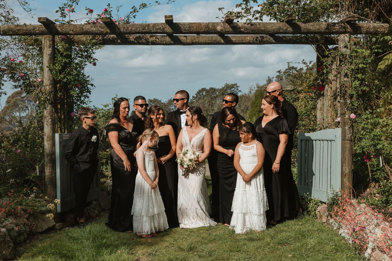 Wedding party poses outdoors in elegant black and white attire against a natural garden backdrop.