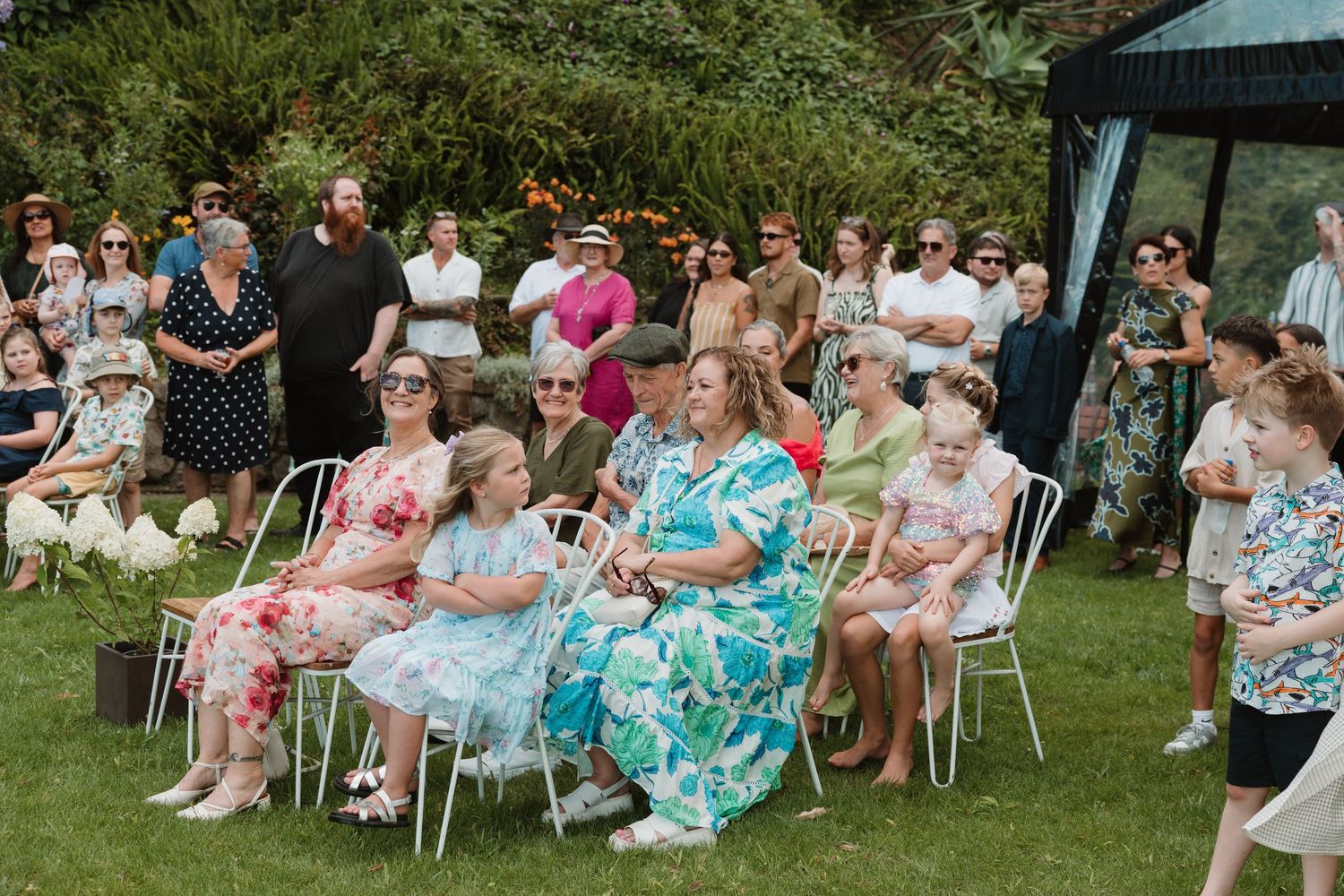 Guests seated on white chairs at an outdoor garden party, enjoying a sunny summer celebration together.