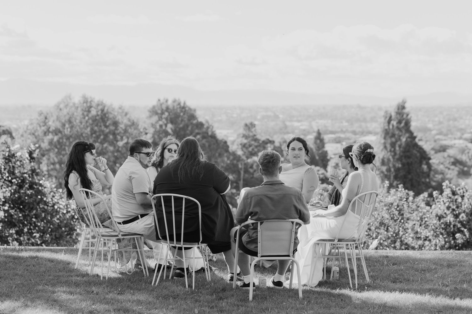 Group of guests seated outdoors at a hillside table enjoying a gathering with scenic countryside views.