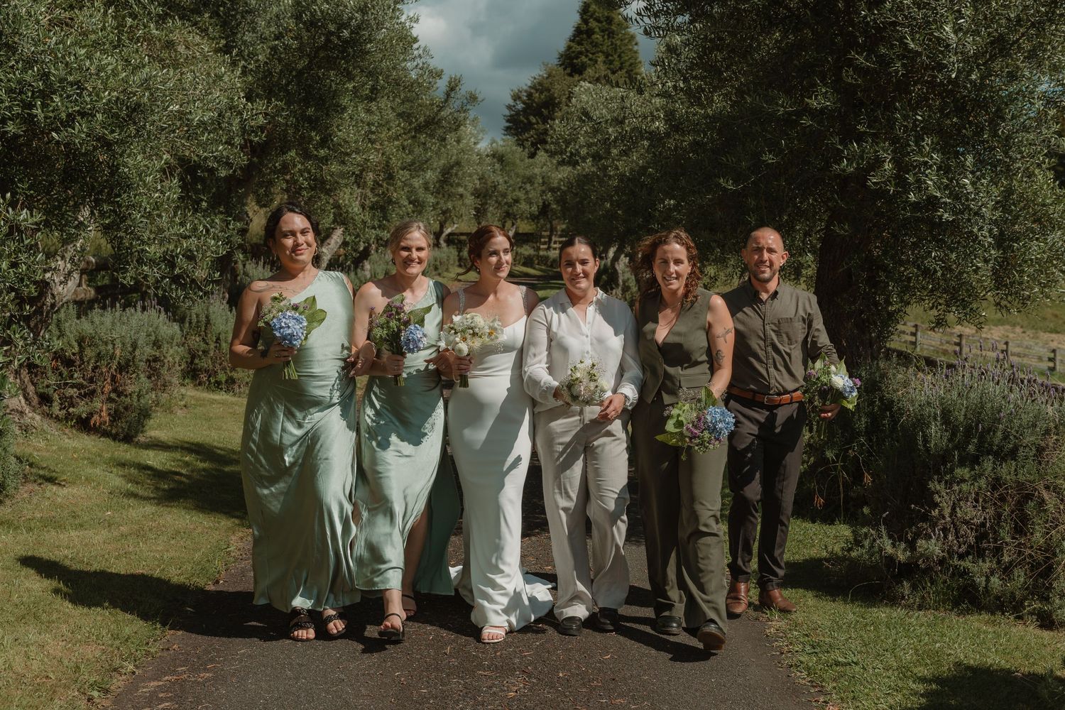 Bride and bridesmaids in mint green dresses walking together on a garden path holding bouquets.