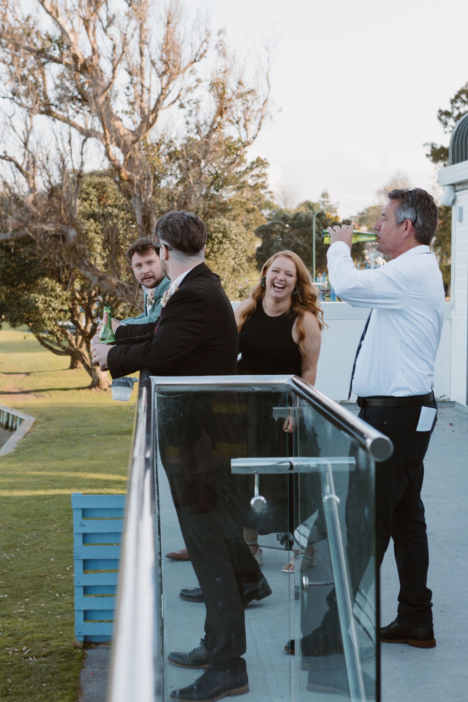 Group leans against a blue railing at sunset during what appears to be a joyful celebration outdoors.