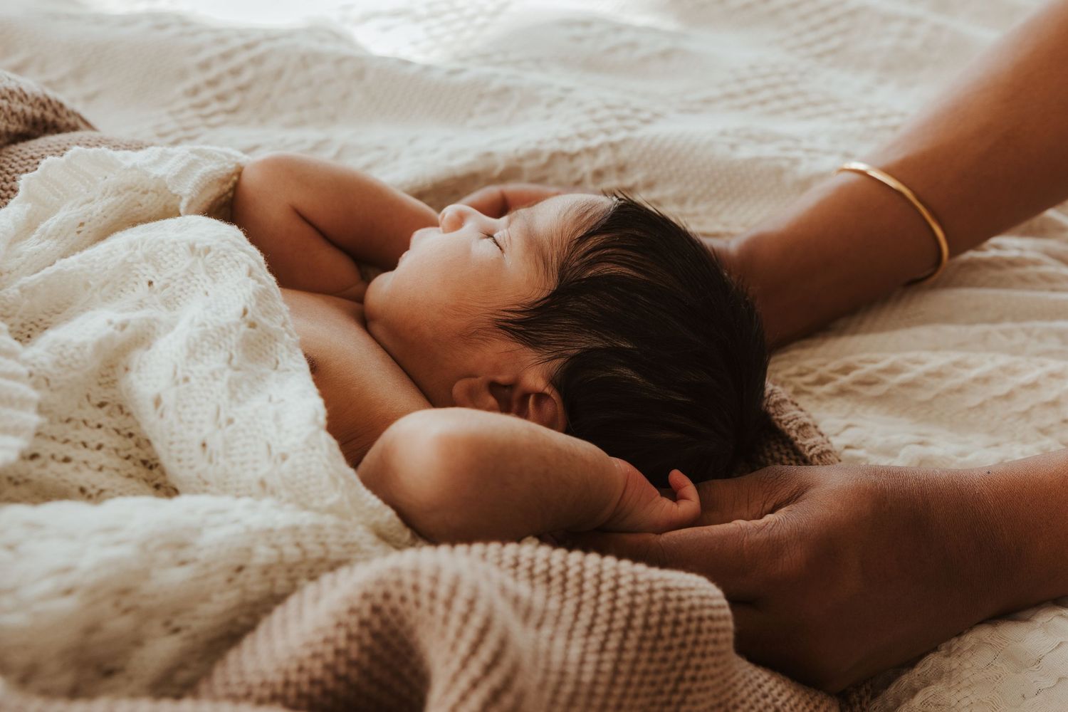 Close-up view of hands tenderly holding a sleeping newborn baby wrapped in a soft white blanket.