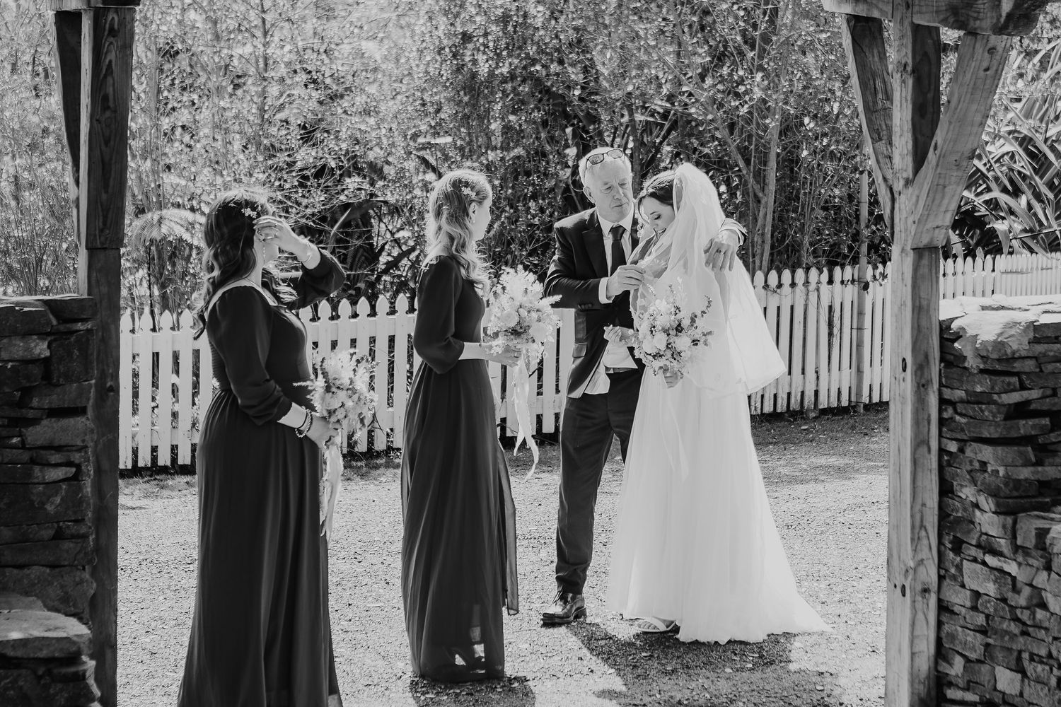 Black and white wedding photos show a series of candid moments on a walkway with a white picket fence.