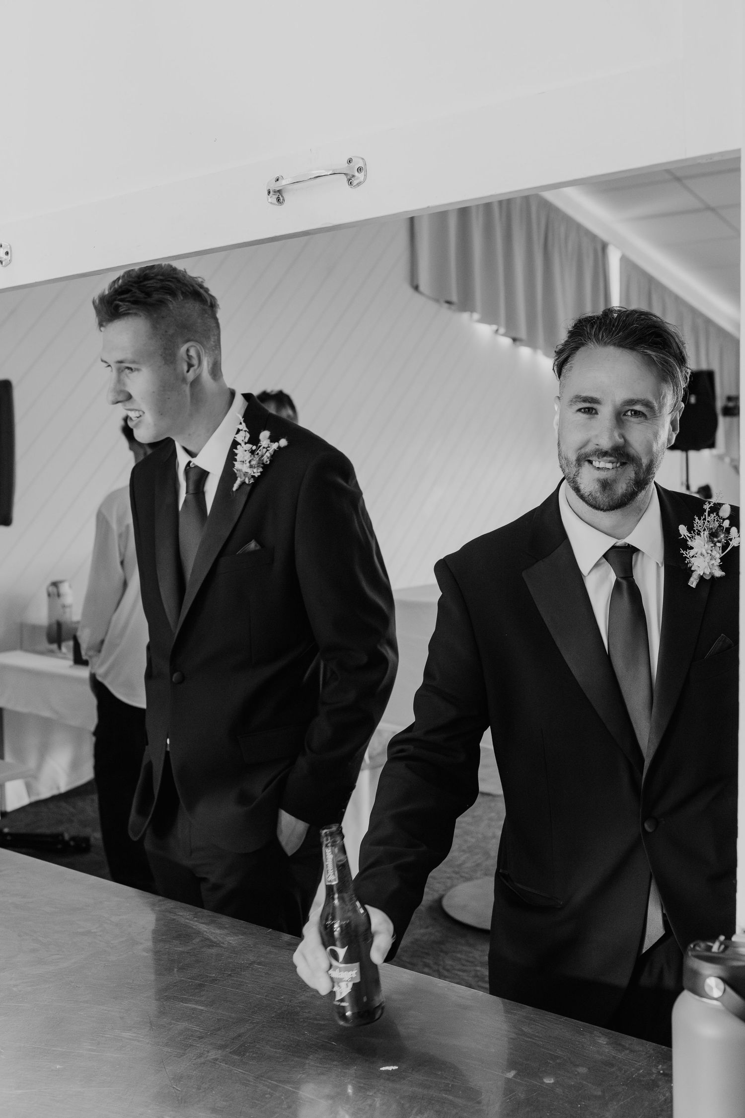 Two men in formal suits standing at a bar during a wedding reception.