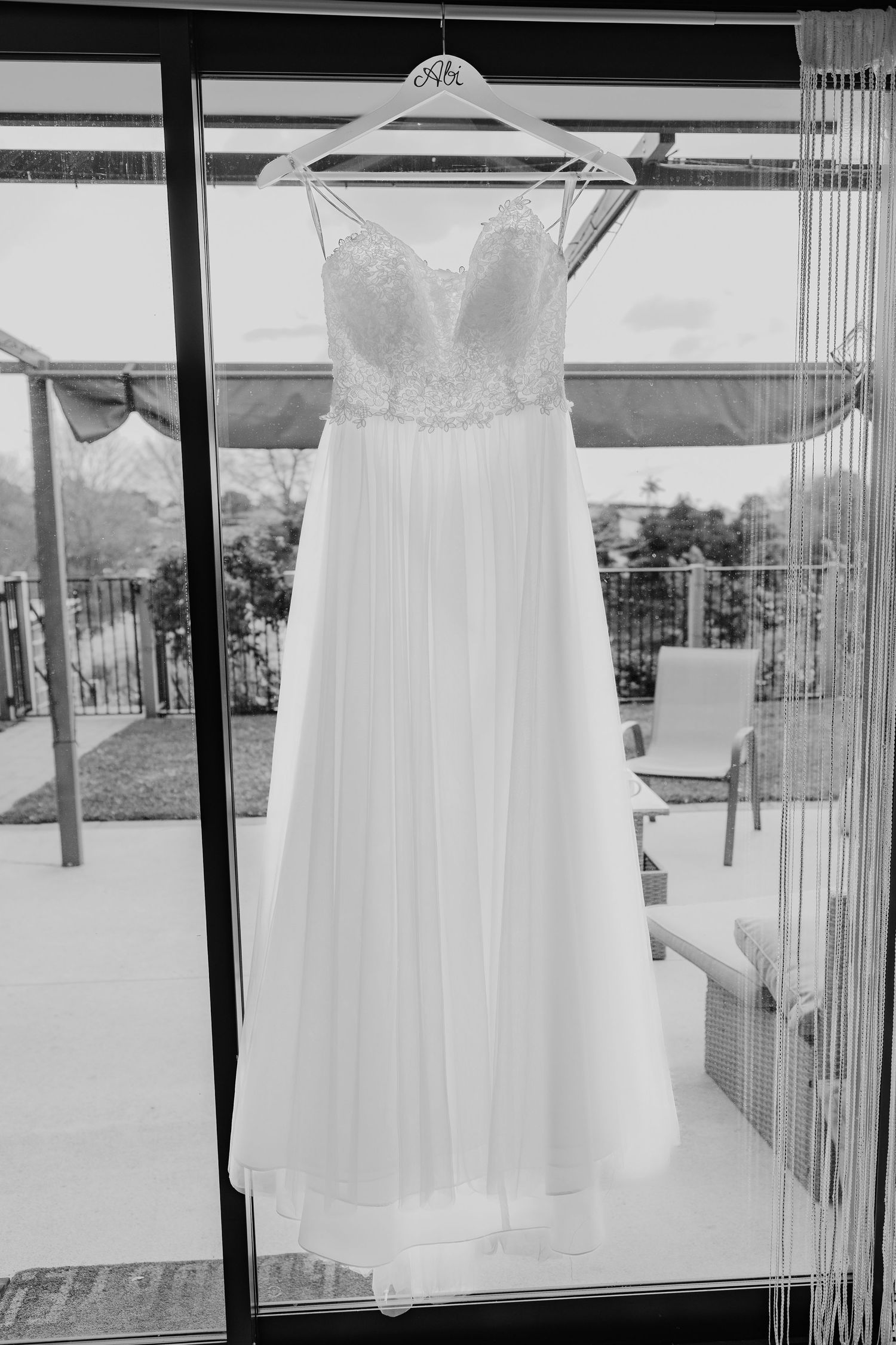 Multiple white wedding dresses hanging in sequence against bright window backdrop.