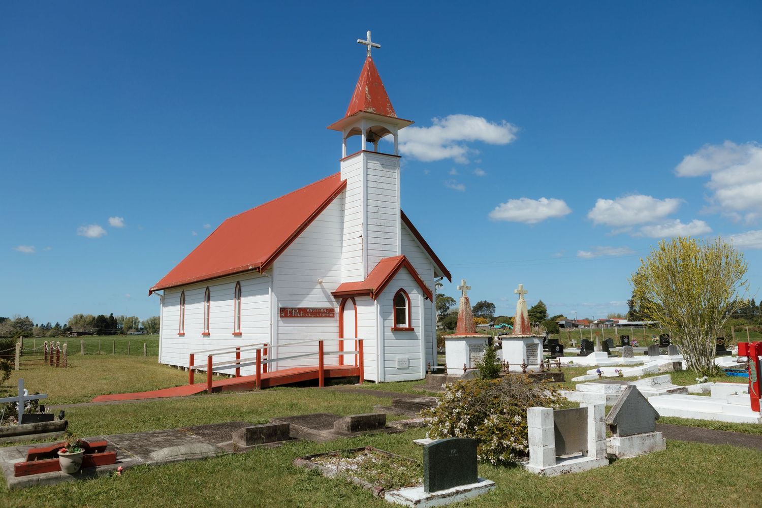 Small white church with red roof and steeple in a rural cemetery setting.