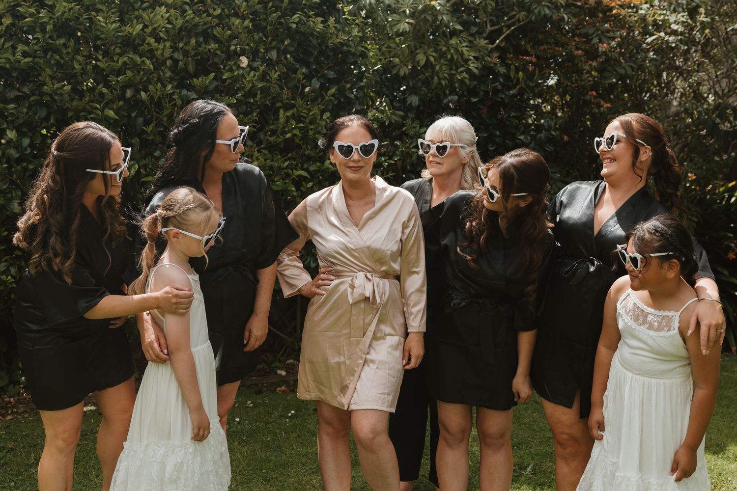 Wedding party members dance and celebrate together outdoors in a garden setting during a summer celebration.