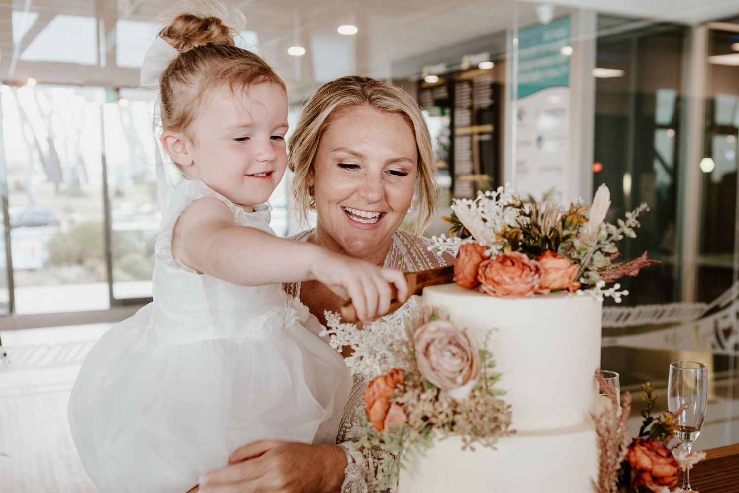 Wedding party shares joyful moments while cutting and serving cake at an elegant indoor reception.