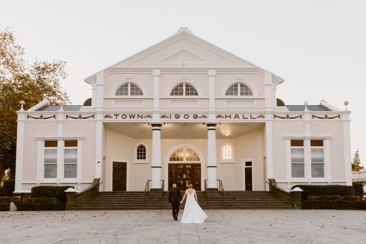 A white colonial style town hall building with arched windows and columns photographed from multiple angles.