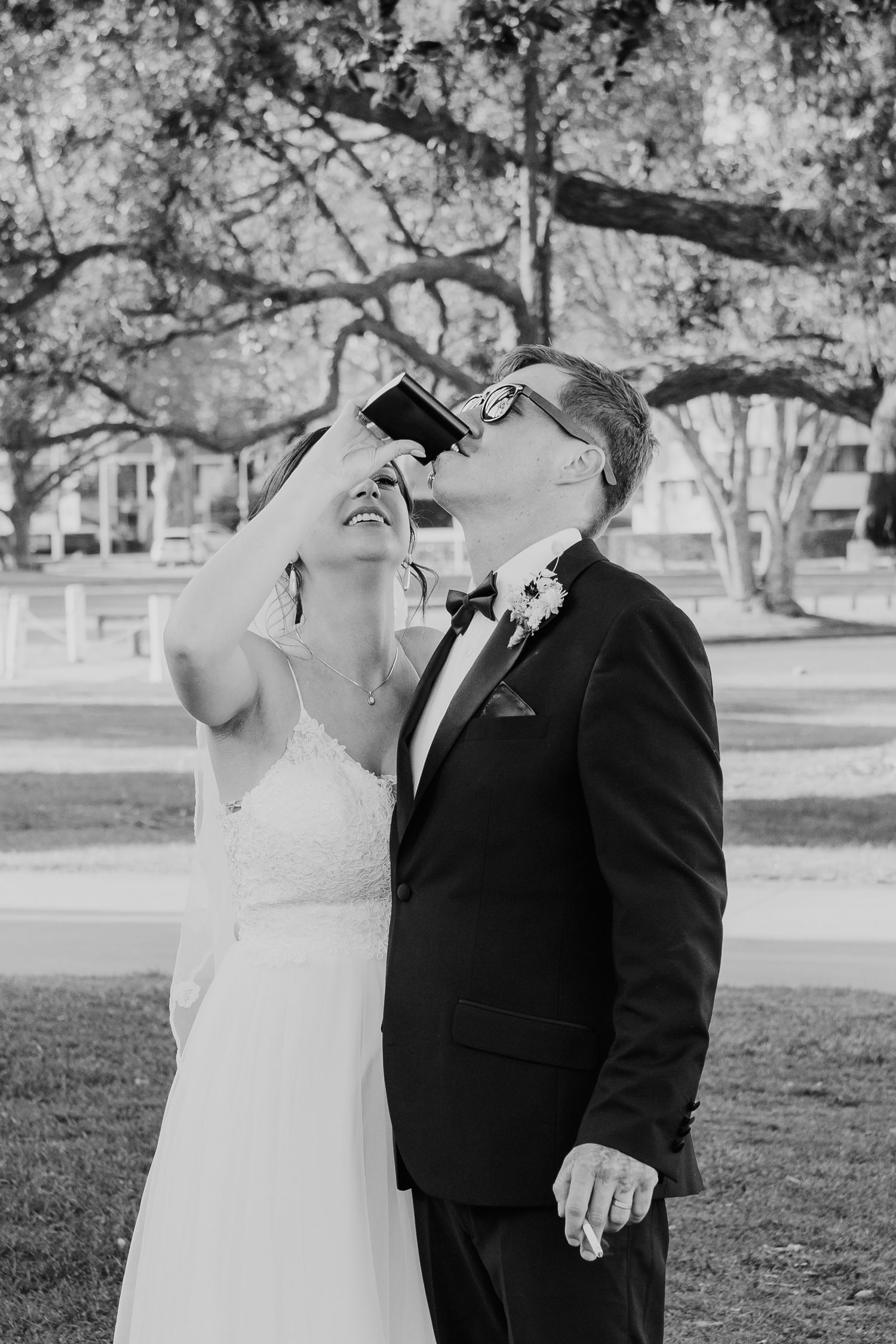 A joyful wedding couple shares a candid moment together outdoors, laughing in a black and white photograph.
