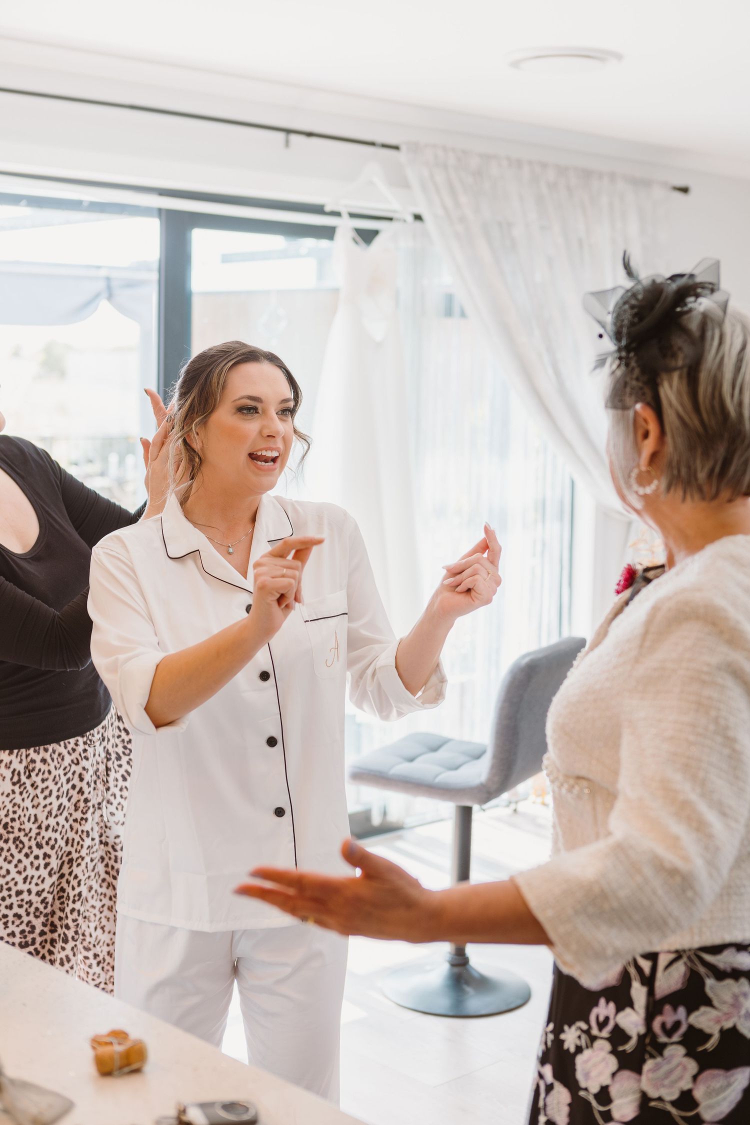 Two people engaged in lively conversation and laughter while wearing white and patterned outfits in a bright room.
