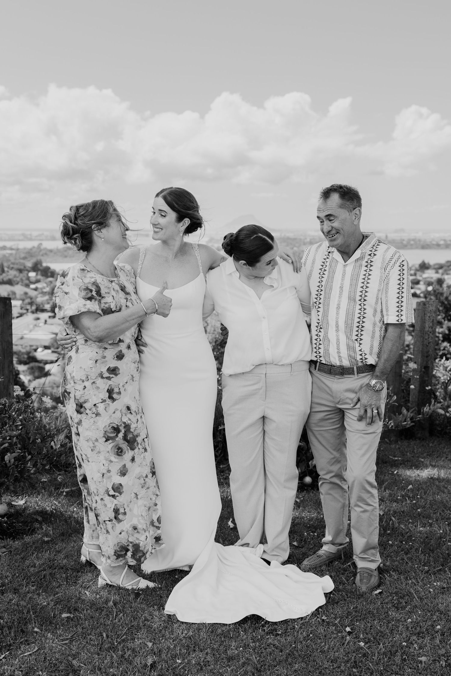Black and white wedding photo of a bride in a white gown with three family members smiling outdoors.