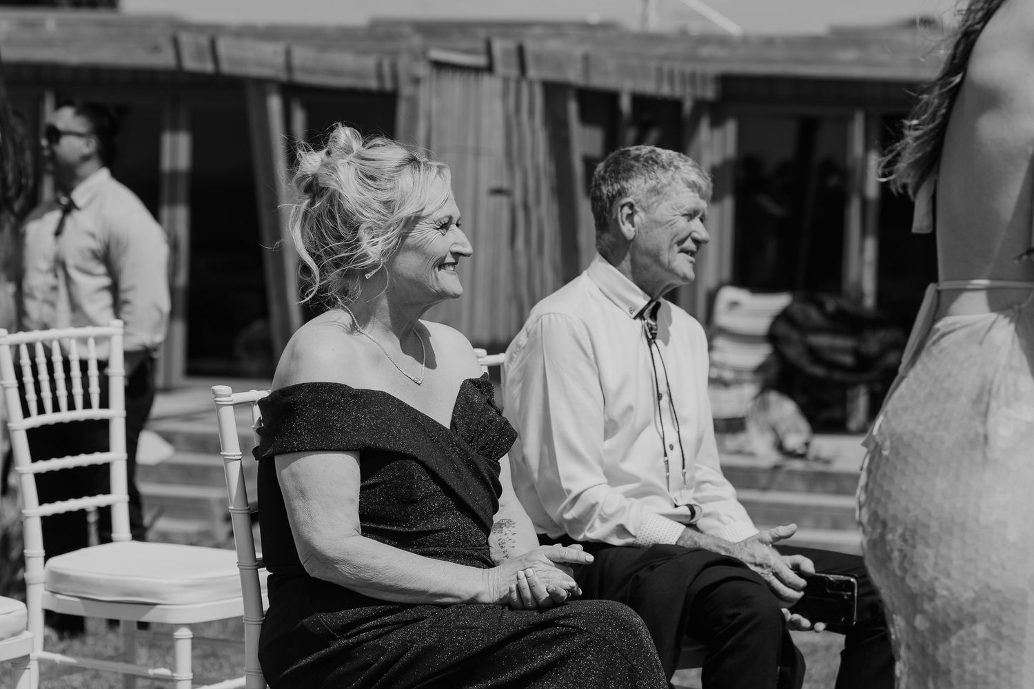 Smiling couple seated at an outdoor wedding ceremony in black and white photography.