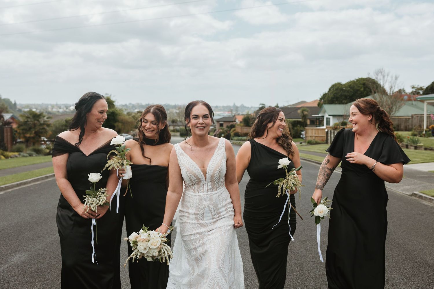 Wedding party wearing black and white attire poses together on a paved road during an outdoor celebration.