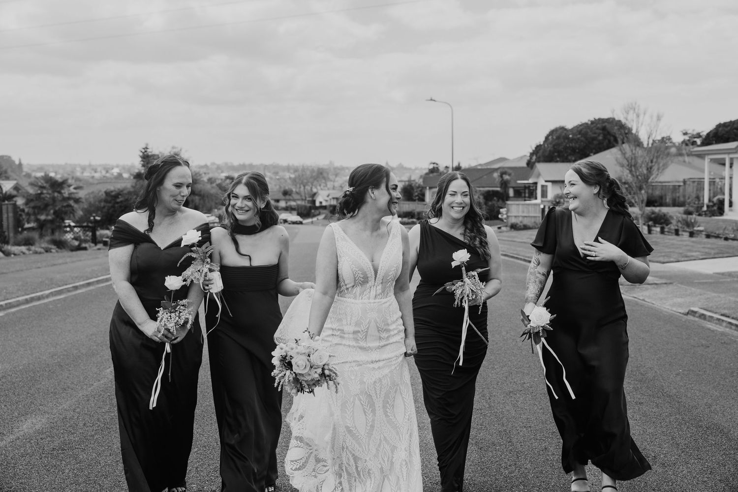 Black and white wedding party walking and laughing together on a paved path outdoors.