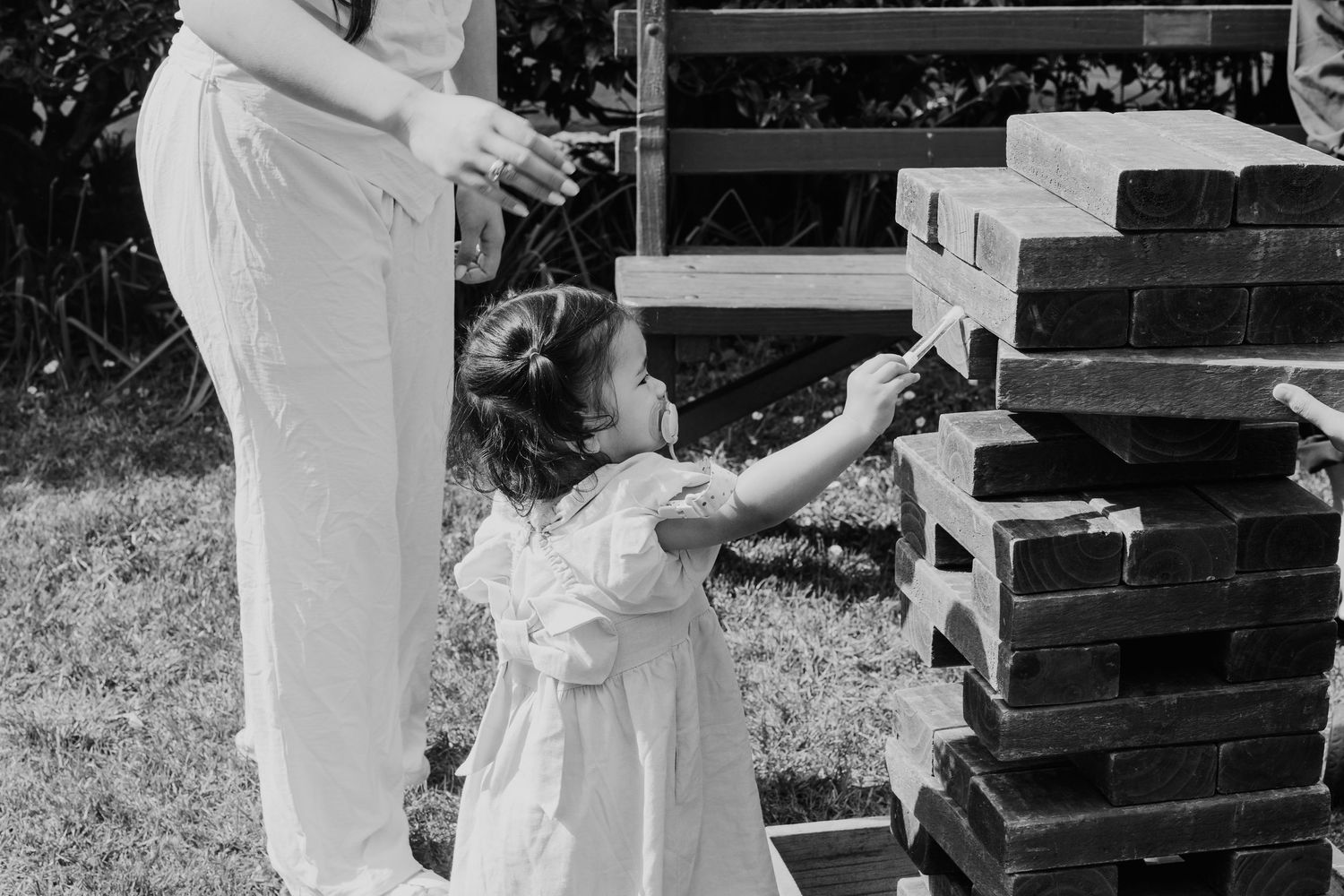A vintage black and white photo showing a child in a white dress reaching up toward wooden steps outdoors.
