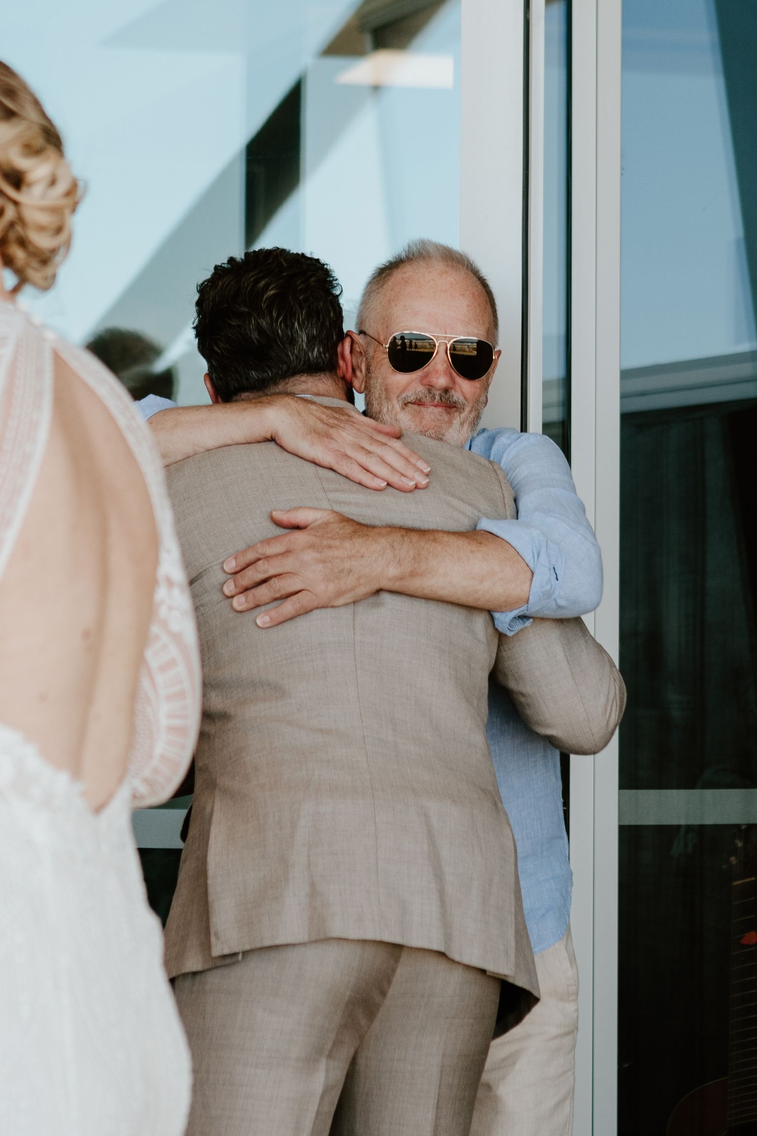 Emotional wedding reception embraces captured in sequence through glass windows. Papamoa Beach Wedding